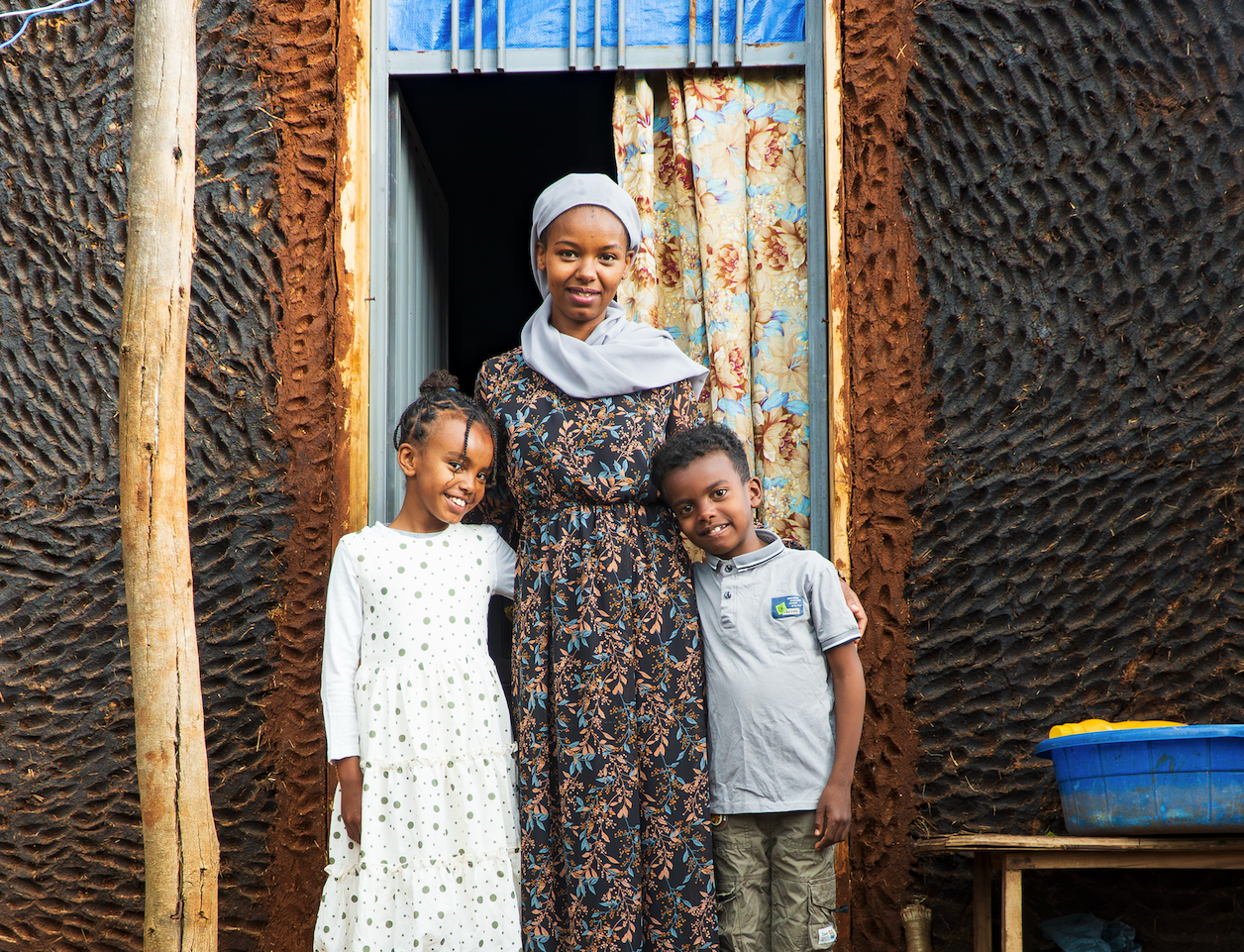 A young mother smiling with her young son and daughter in the doorway of their home