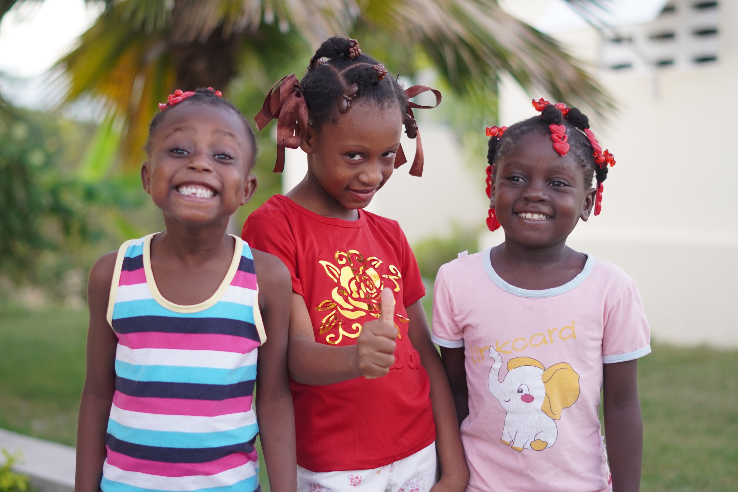 Three little sisters smiling together and giving a thumbs-up