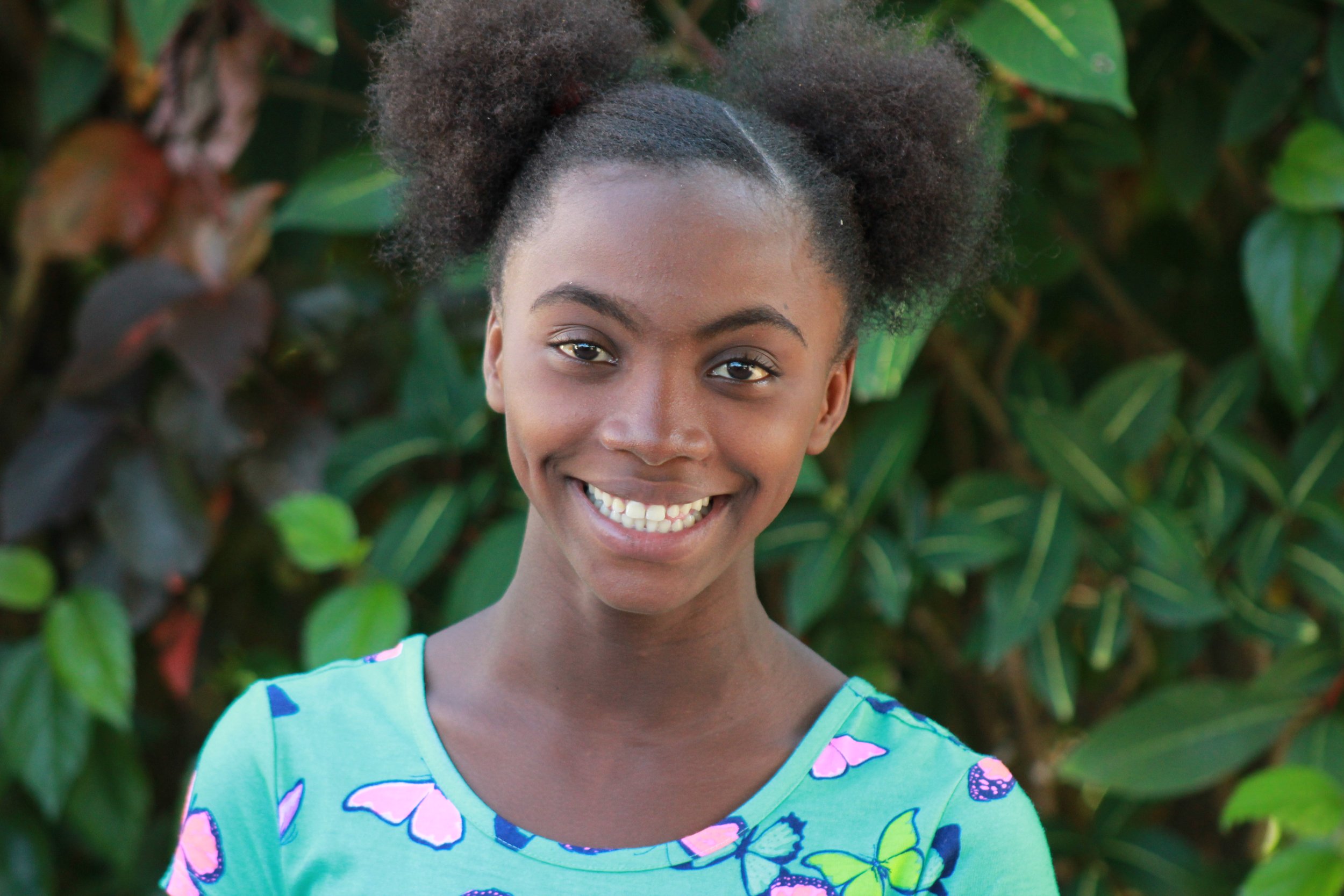 Young Haitian girl smiling in a blue dress with greenery in the background