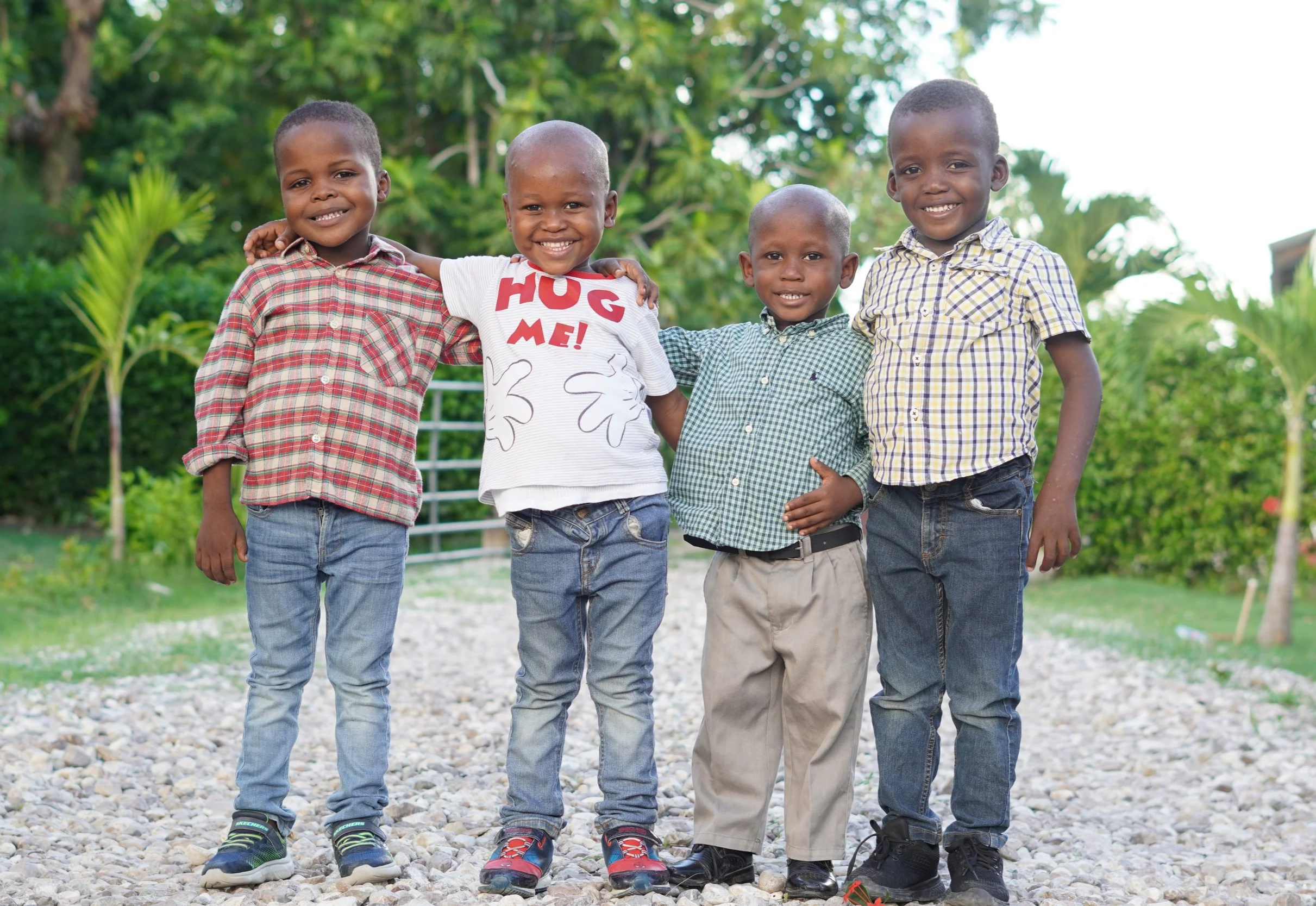 Four little Haitian boy brothers smile and have their arms around each other outside