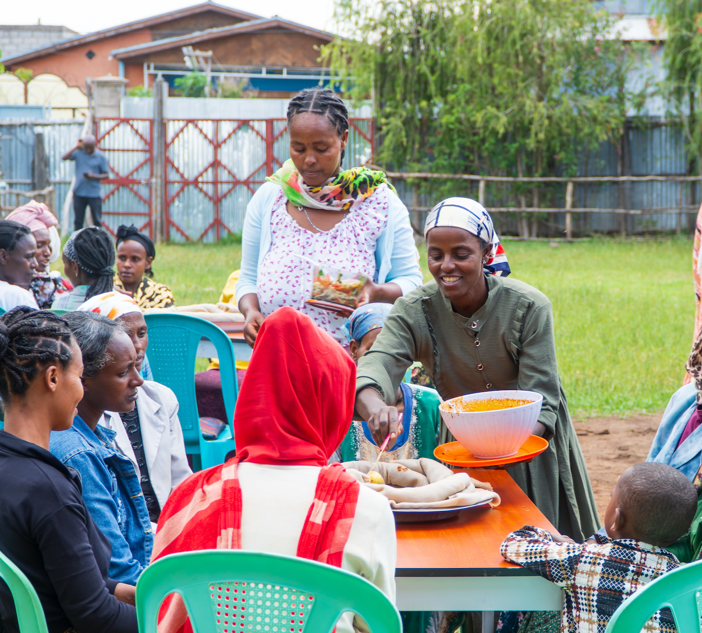 An Ethiopian woman smiles as she serves food to other women at a table outside