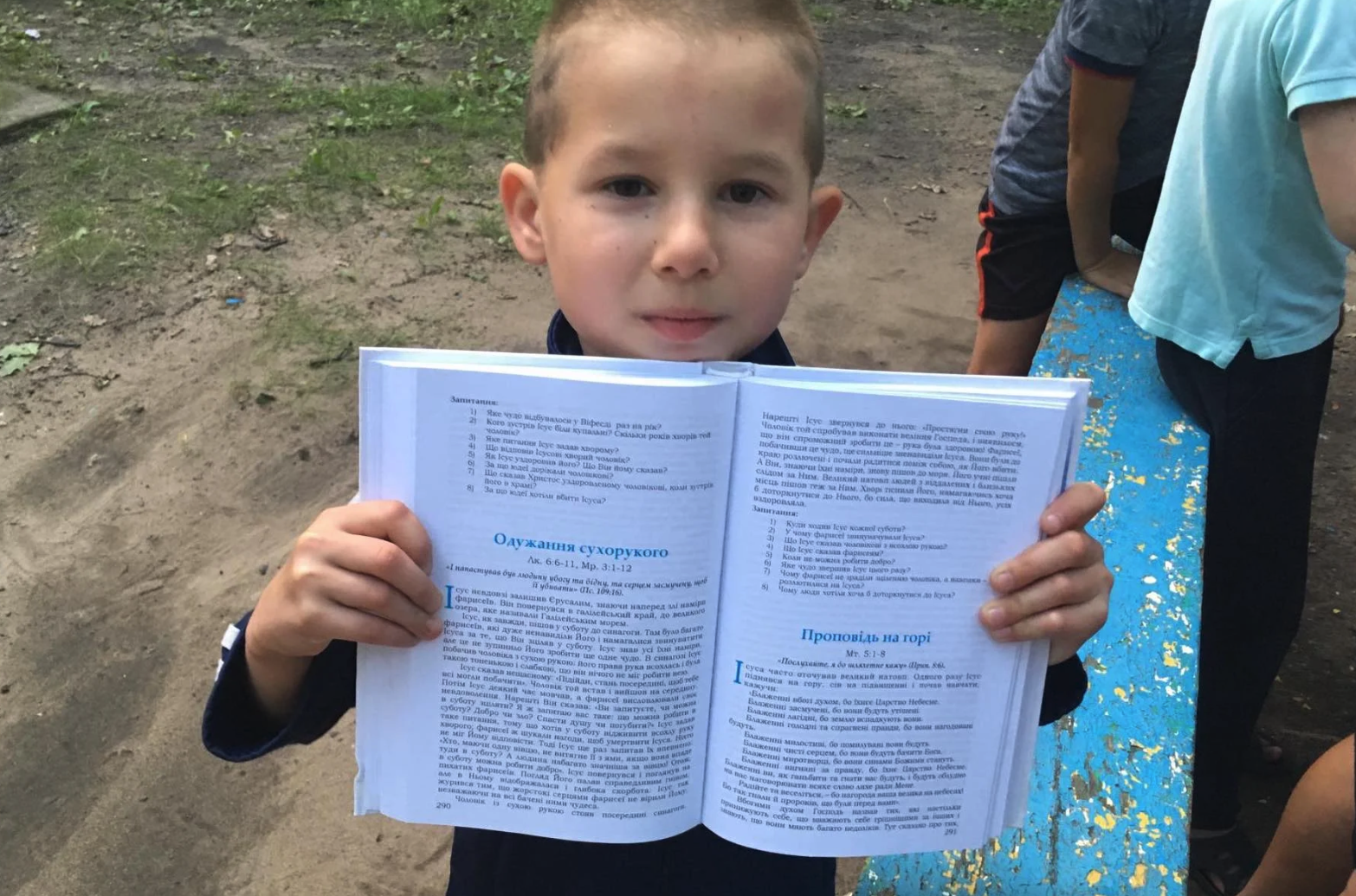 A young Ukrainian boy smiles and hold up his opened Bible outside