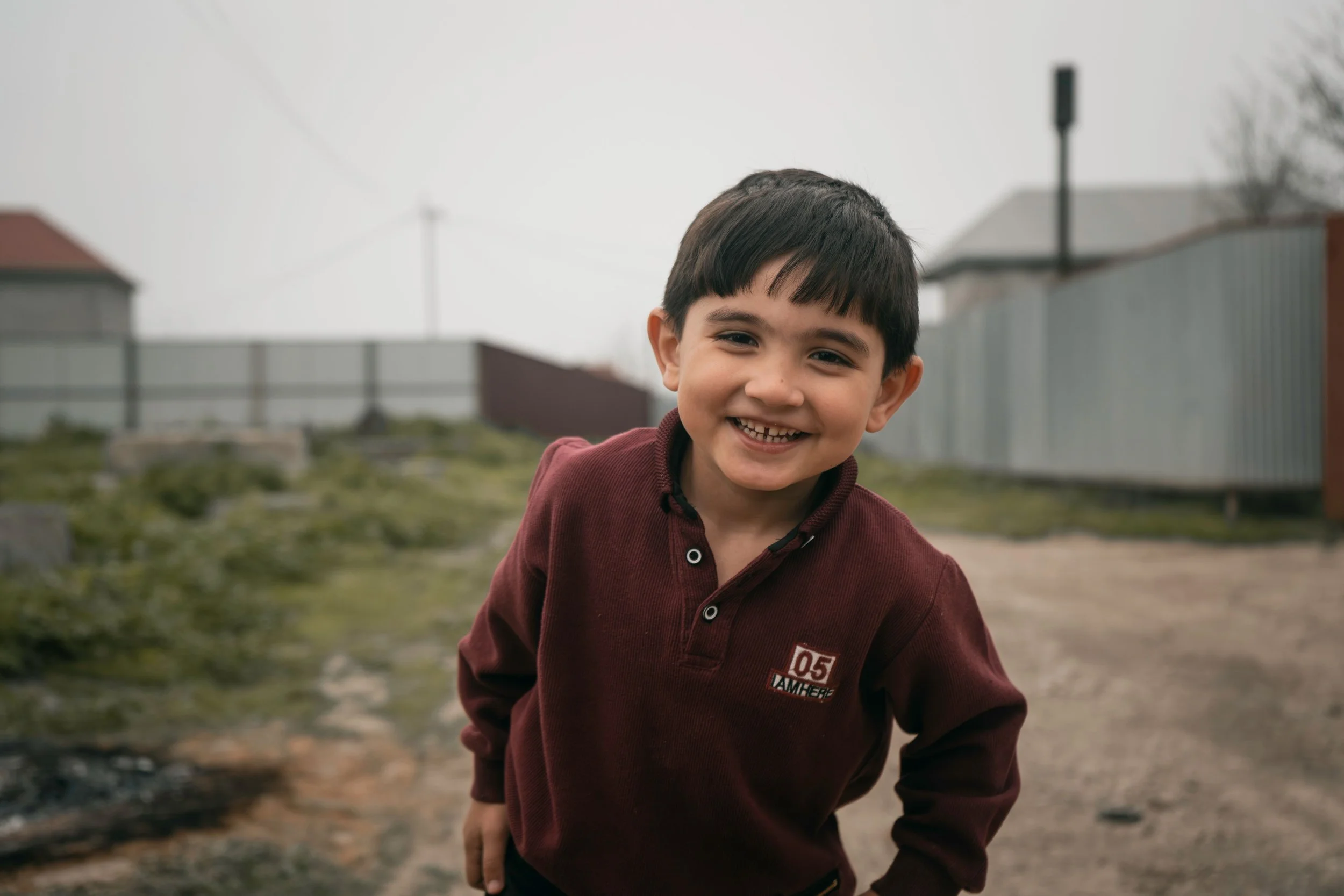 Little Ukrainian boy with dark hair and dark eyes smiling outside on a cloudy day with tin buildings in the background
