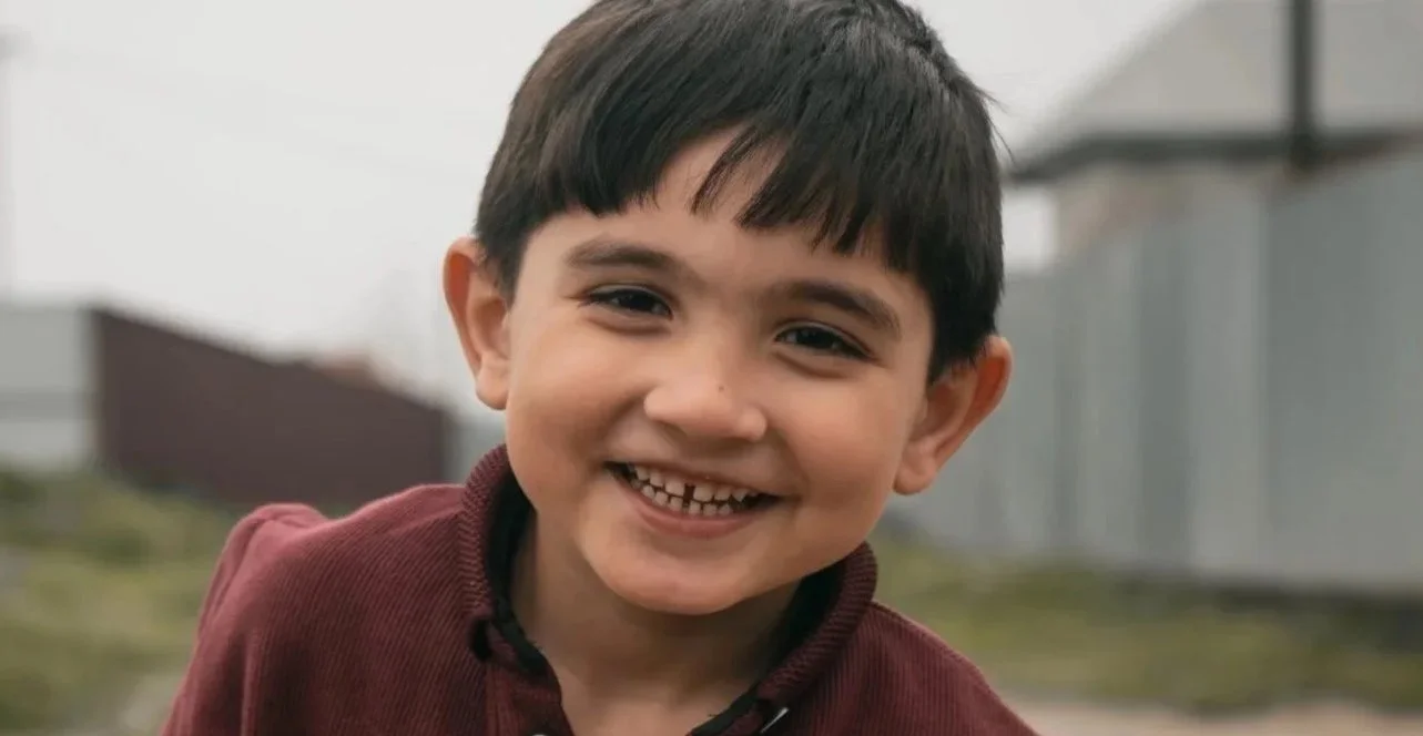 A little Ukrainian boy with black hair and eyes smiling outside