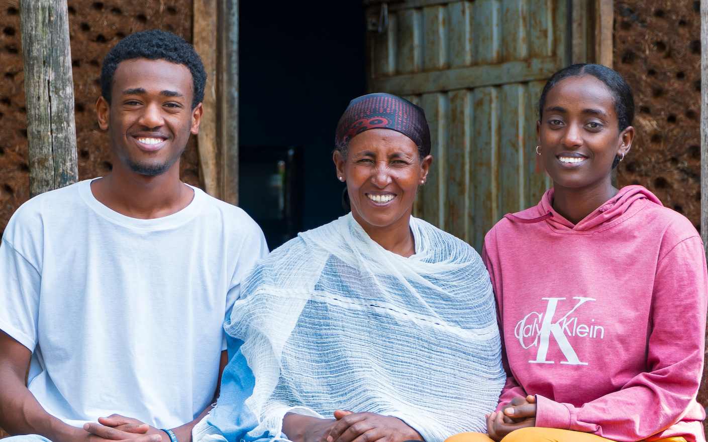 An Ethiopian mother sits between her son and daughter, they all smile in front of their home
