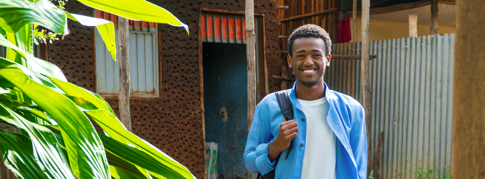 A young Ethiopian man leaving his home and smiling with his backpack over his shoulder to go to school