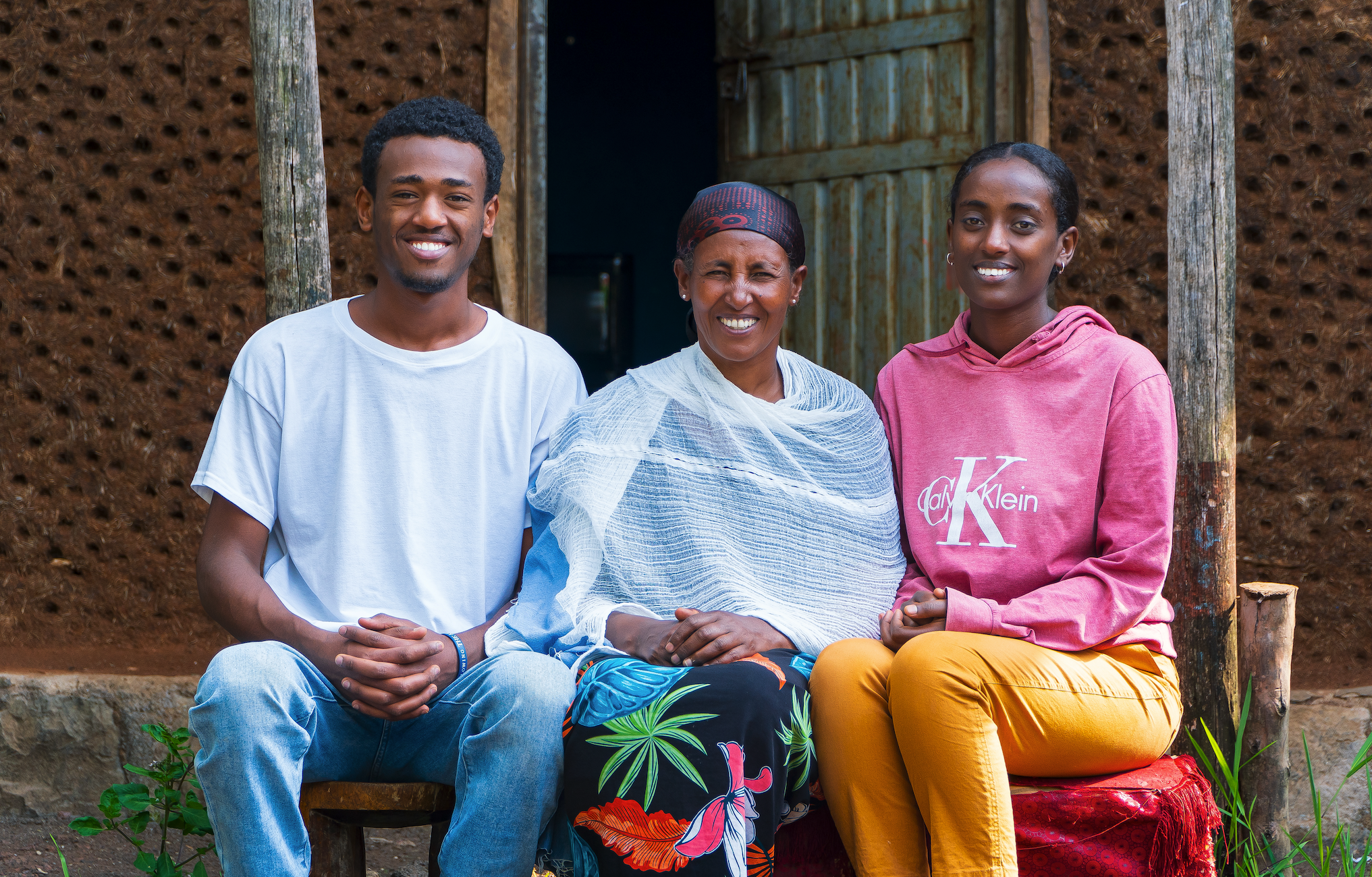 An Ethiopian mom smiles with her son and daughter in front of their home