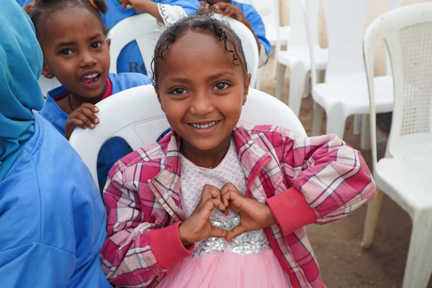 A young Ethiopian girl in a pink dress smiling and making a heart with her hands