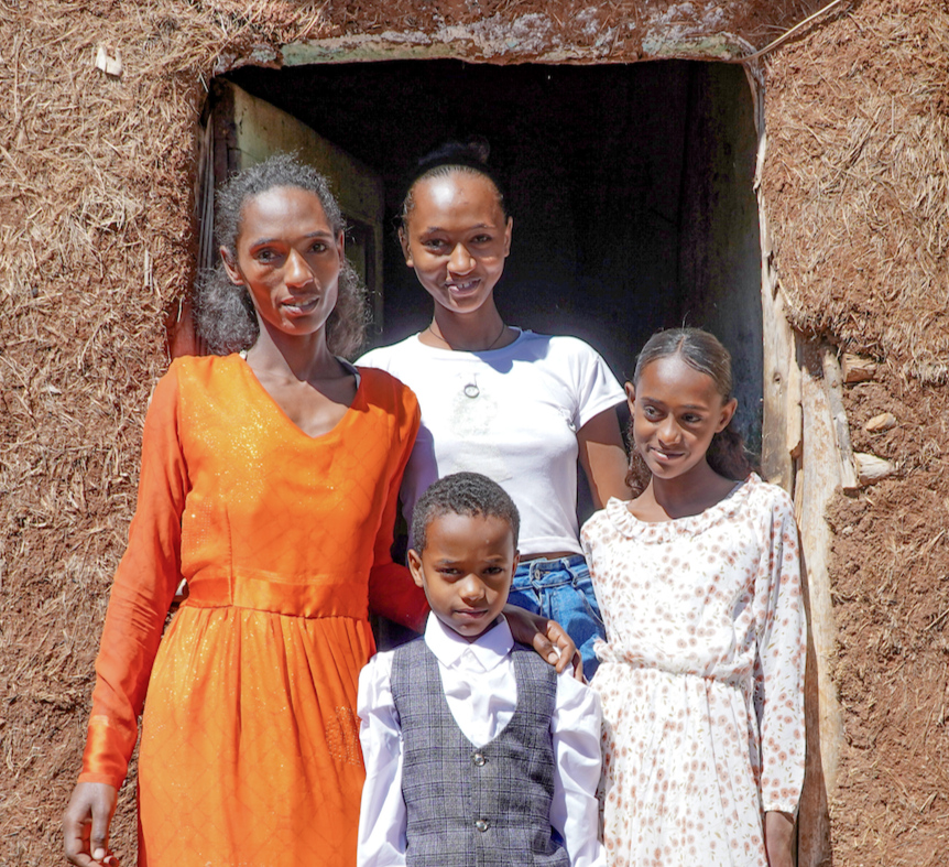 Ethiopian mother with her two daughters and one little son stand together and smile in the entrance to their home