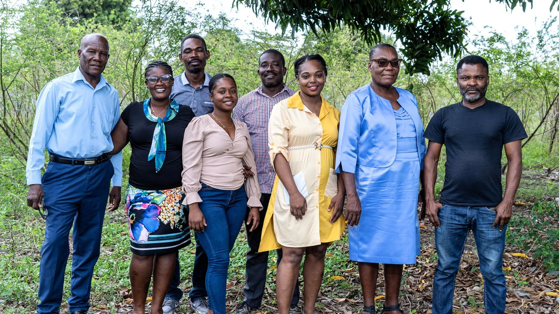 A group of eight Haitian men and women smiling and standing together outside
