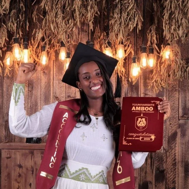 Konjit proudly showing her diploma while wearing her cap and pumping her fist