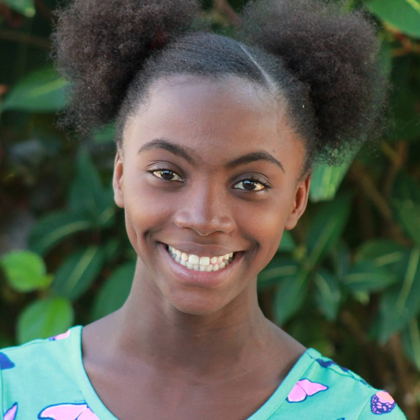 Young Haitian girl smiling in a blue dress with greenery in the background