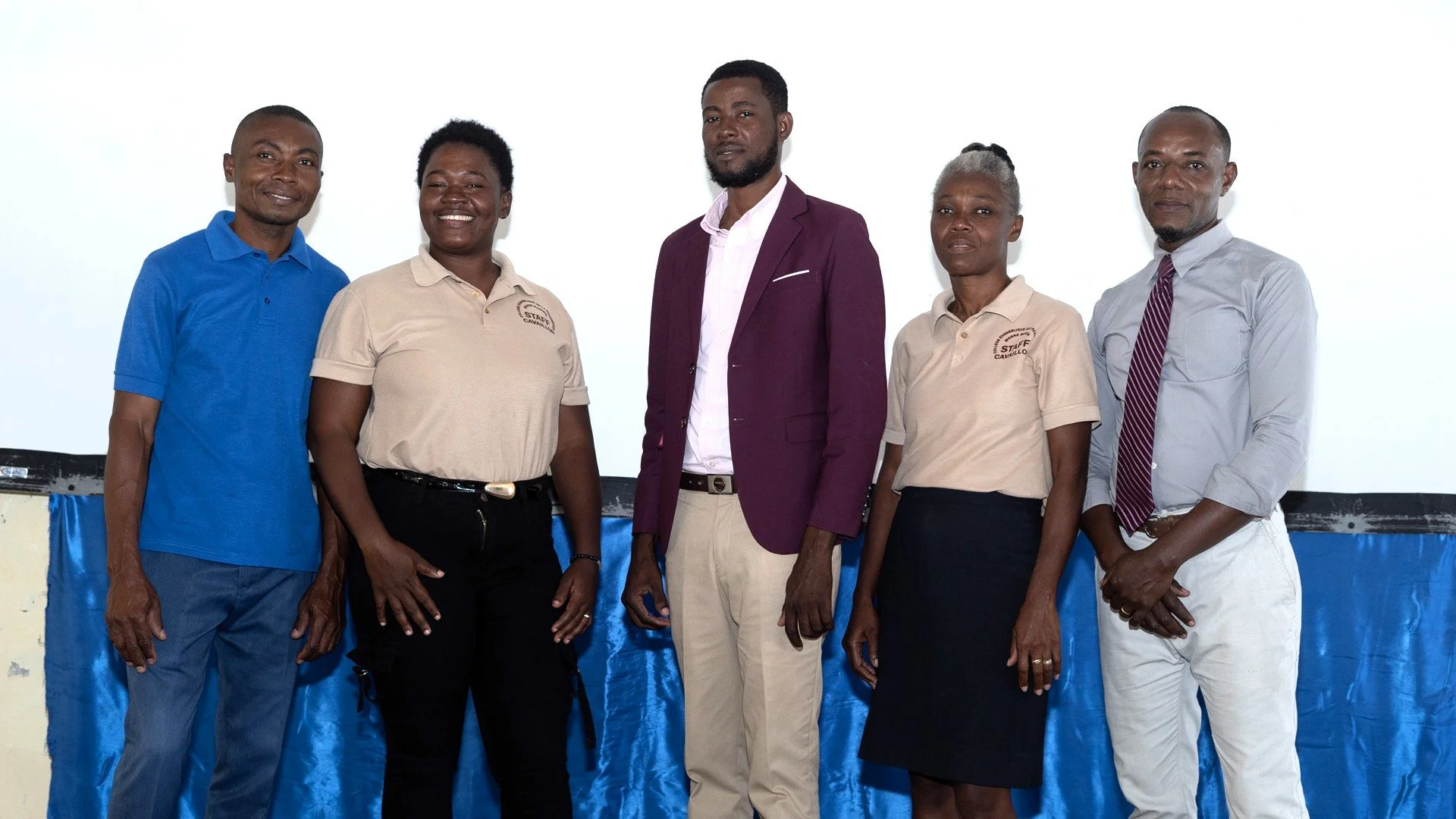 A group of five Haitian men and women smiling and standing together in front of a bright white and blue wall