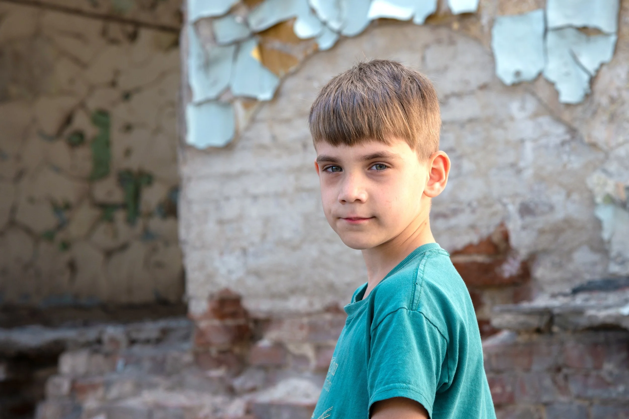 A young Ukrainian boy smiles softly outside with stone buildings behind him