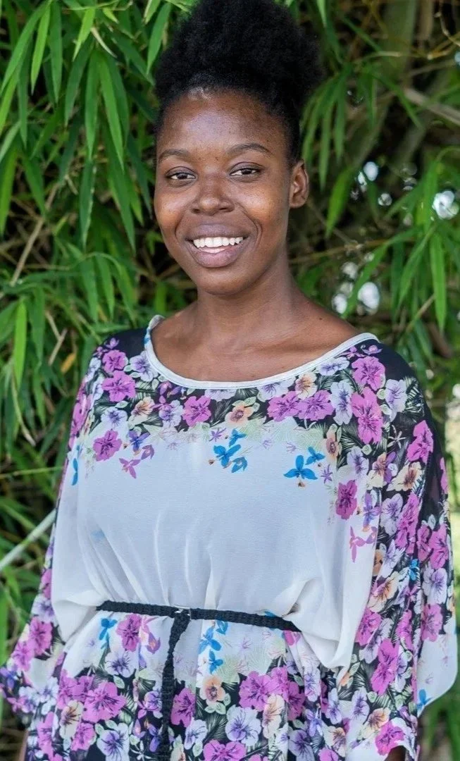 Young Haitian woman smiling outside in front of greenery with a floral shirt on