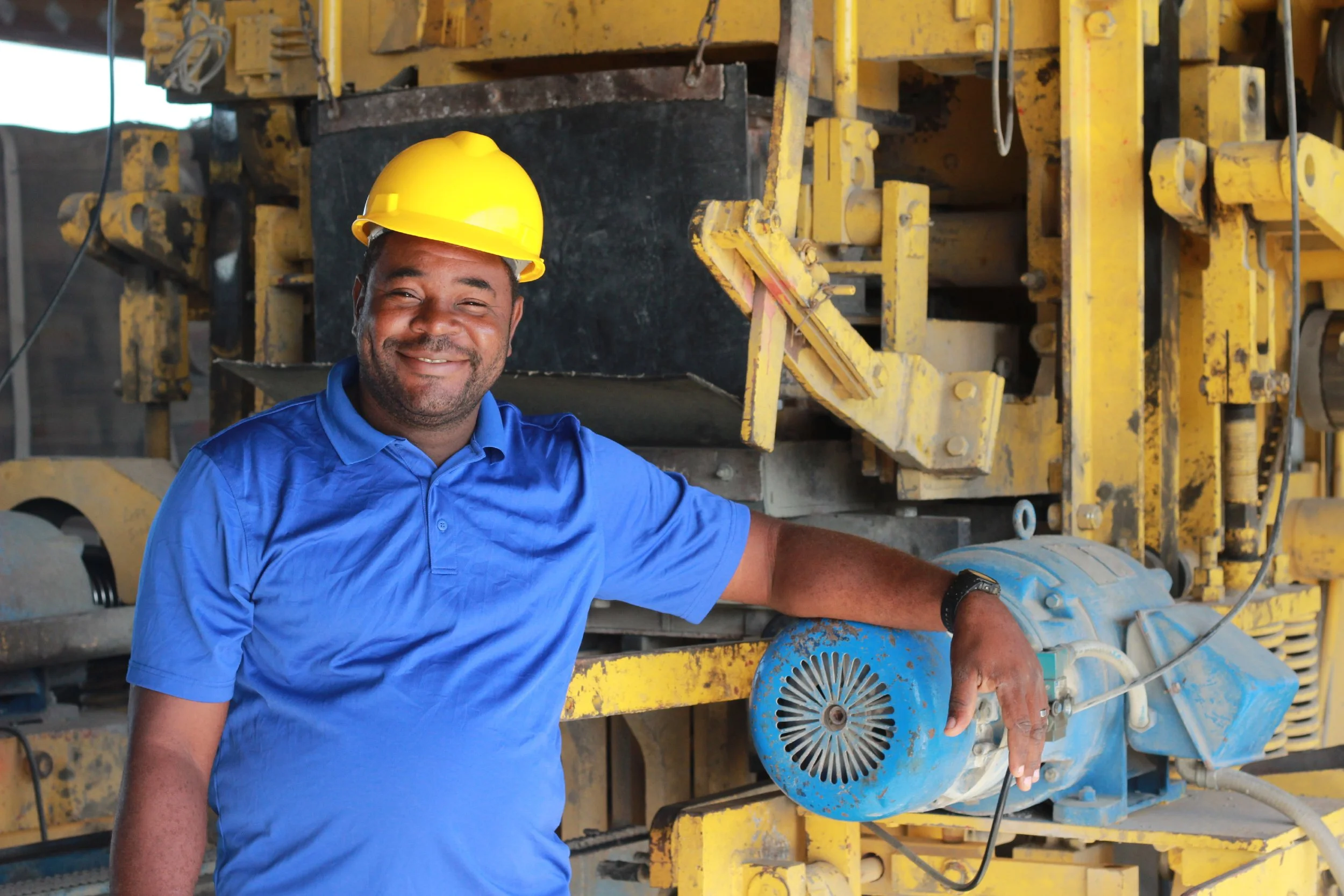 Haitian man in a hard hat smiling and standing next to machinery