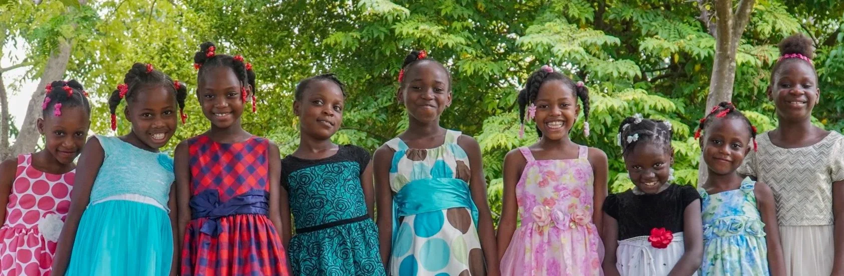 A group of nine sisters from the Naomi Home of Hope smile together in dresses outside