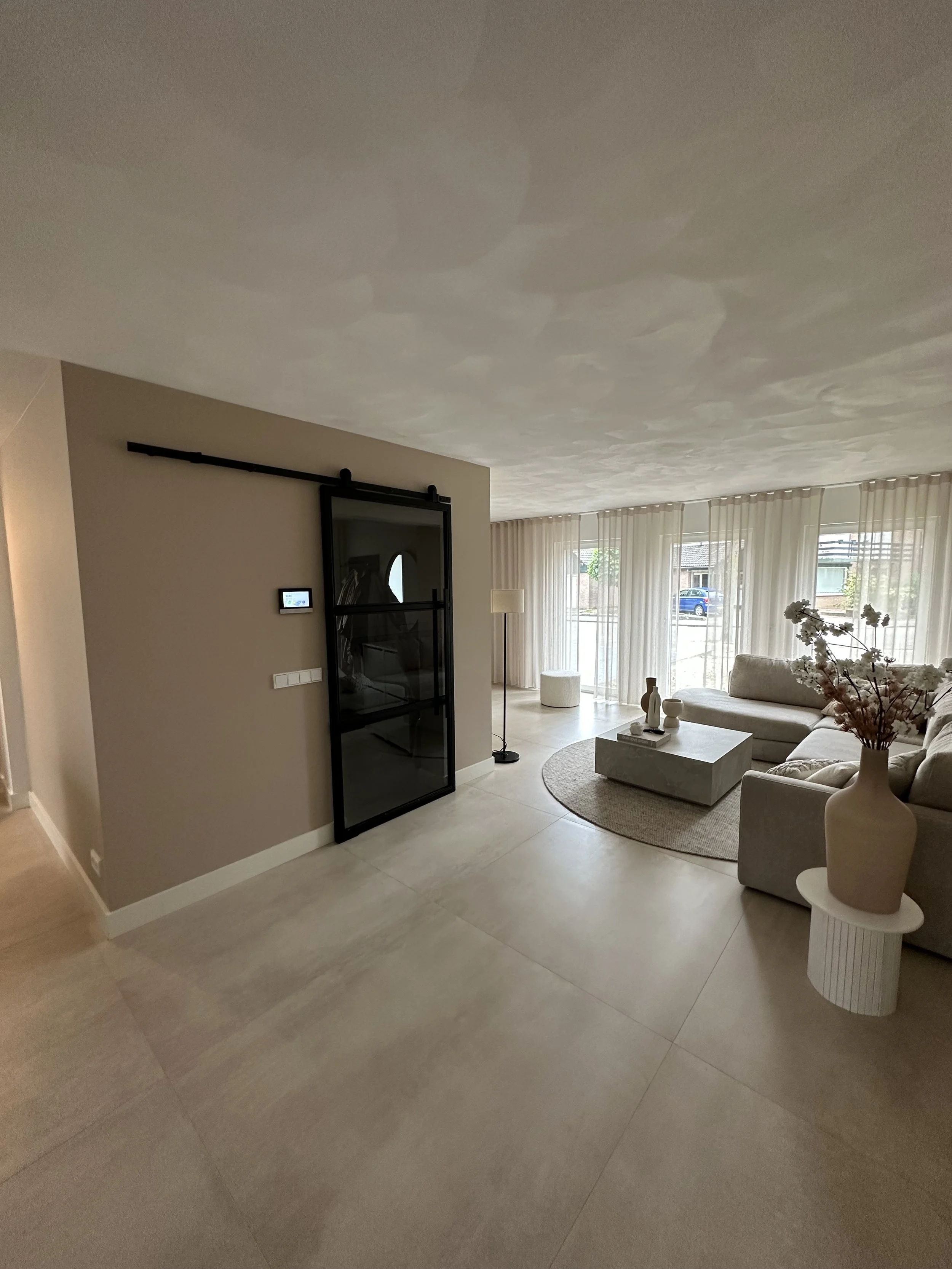Modern living room with beige sofa, round rug, and large windows with sheer curtains.