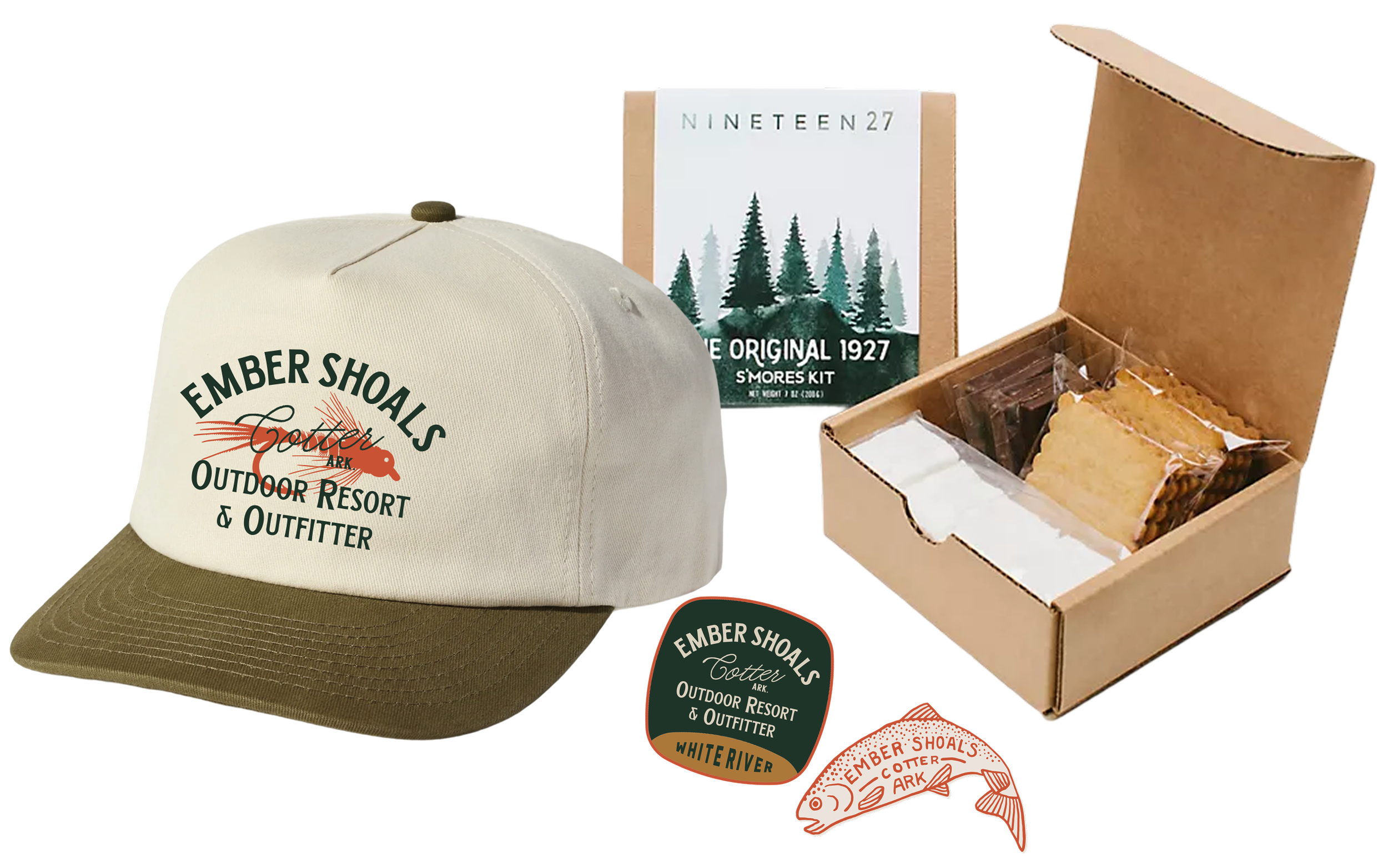 A beige cotton baseball cap with green and red embroidery that reads 'EMBER SHOALS Cotter, Arkansas OUTDOOR RESORT & OUTFITTER', a box of s'mores ingredients with graham crackers, marshmallows, and chocolate, and a sticker and pin featuring a fish with the text 'EMBER SHOALS Cotter Arkansas'.