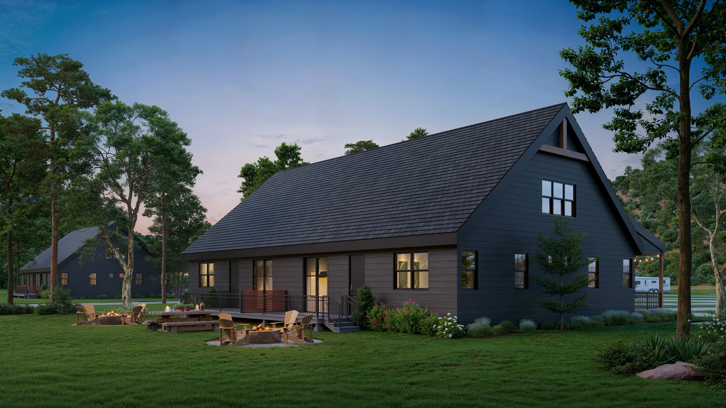 Modern black house with illuminated windows surrounded by green trees and a well-maintained lawn during early evening, with a backyard firepit and outdoor seating area.