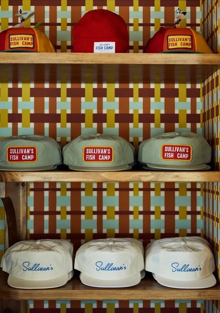 Three white baseball caps with 'Sullivan's' embroidered on them, placed on a wooden shelf.