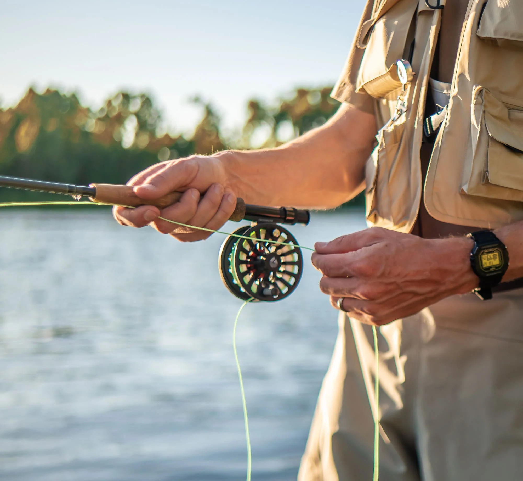 Close-up of person holding a fly fishing rod near a body of water during daylight hours.