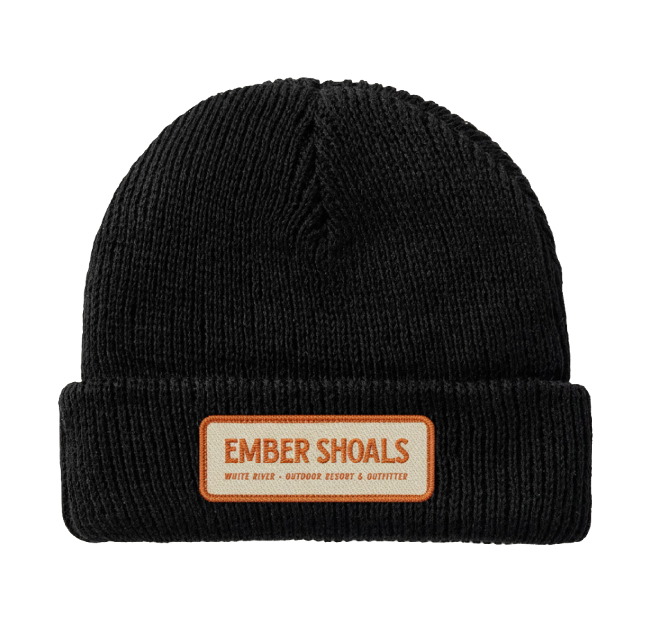 Black knit beanie hat with a rectangular orange and white patch on the front that reads "EMBER SHOALS" and "WILD RIVER - OUTDOOR ESCORT & OUTFITTER".