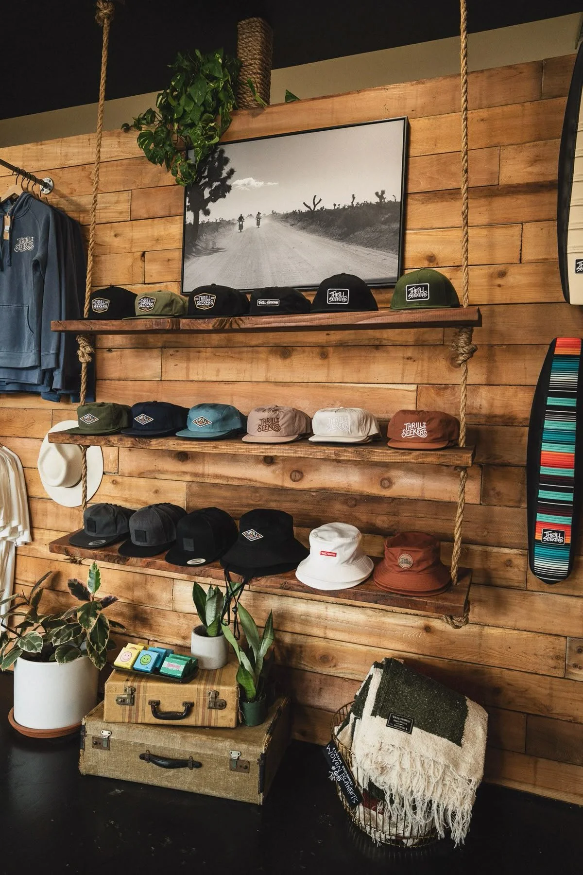 Display of various hats on wooden shelves and a black-and-white poster of a desert scene with two motorcyclists riding on a dirt road, in a store with wooden walls and decor.