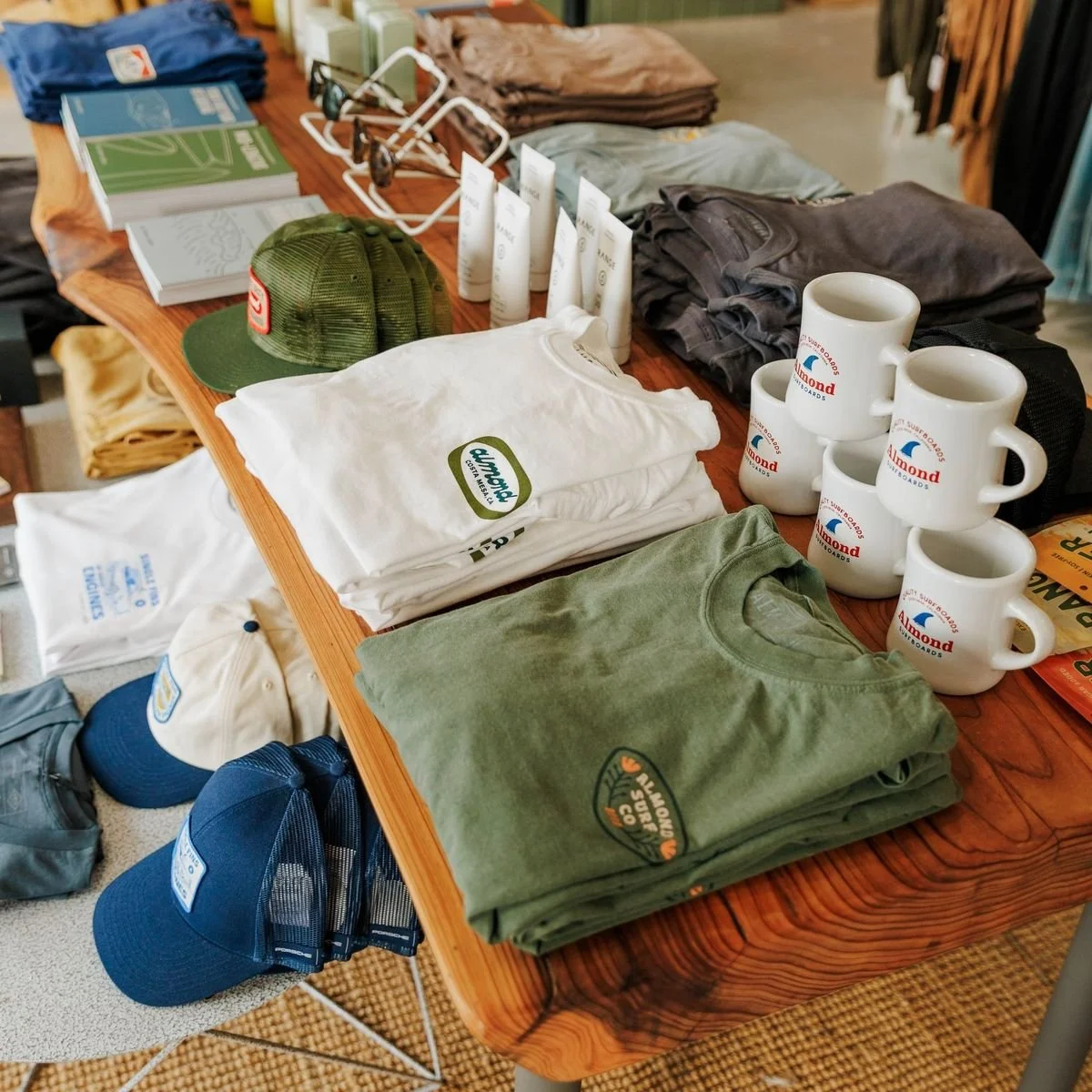 Display of various merchandise including T-shirts, caps, mugs, and promotional items on a wooden table.