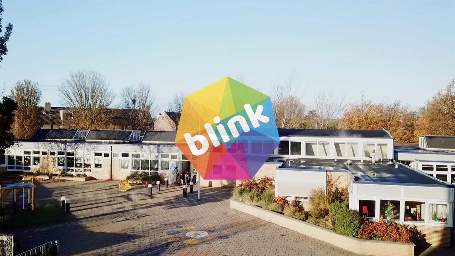 A school building with a courtyard, trees with fall foliage, and a colorful