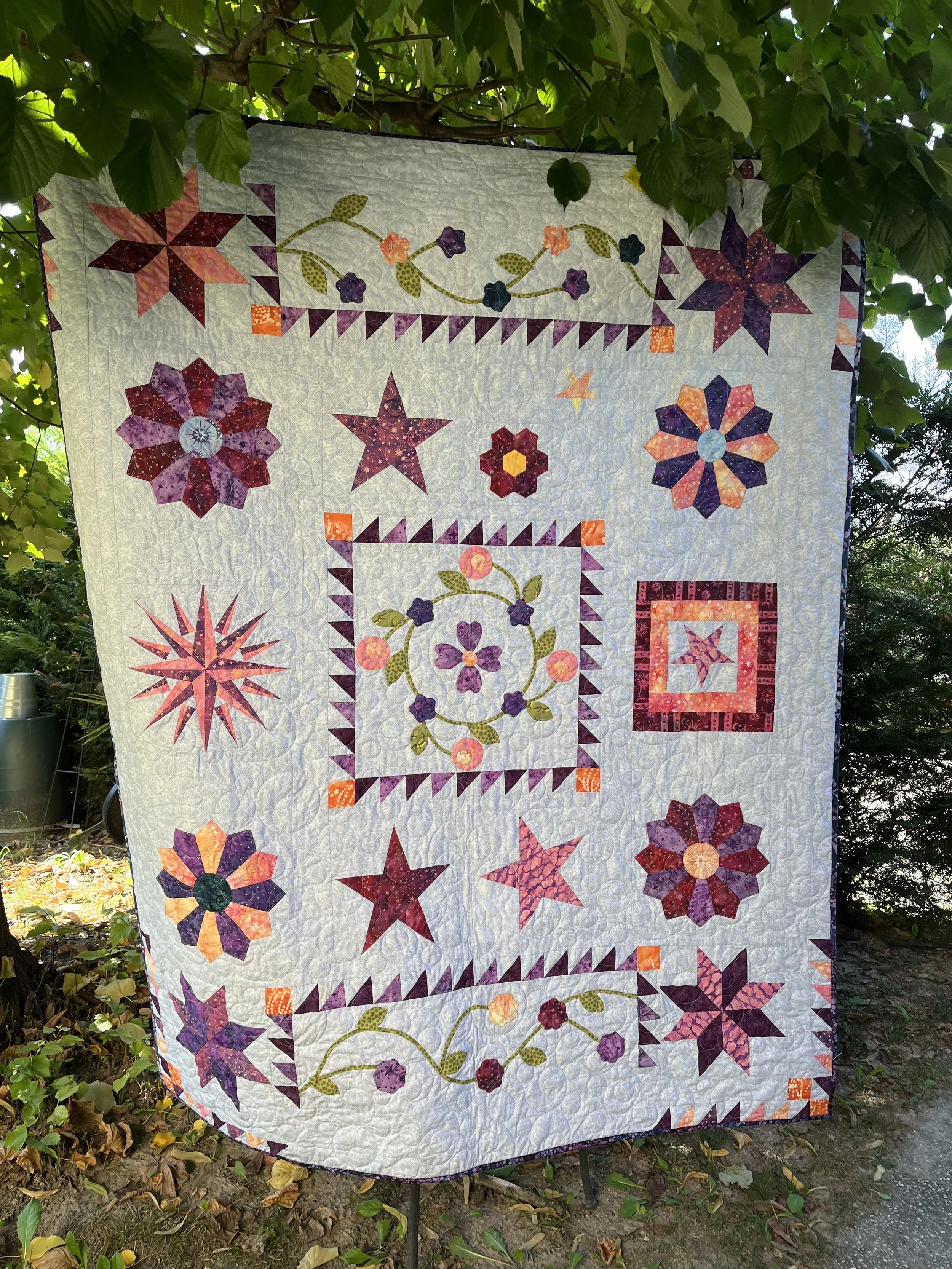 Un coperta ricamata con motivi floreali e stelle, appesa tra gli alberi