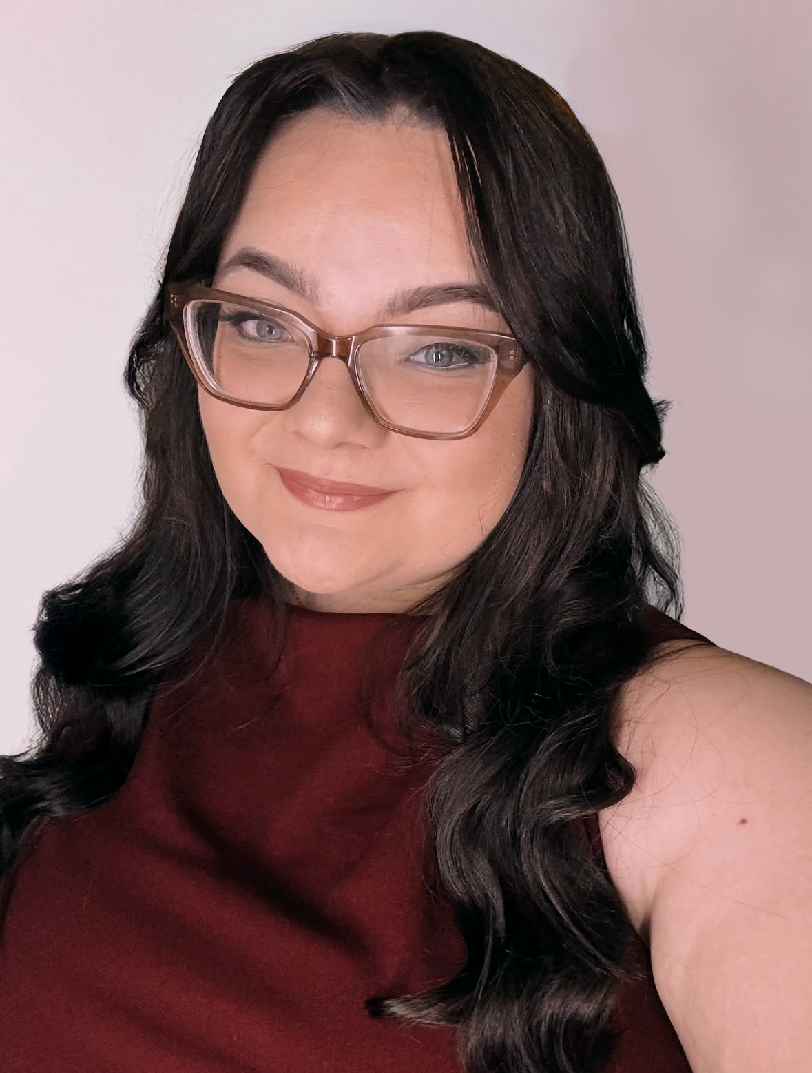 A woman with long dark wavy hair wearing glasses and a sleeveless burgundy top, smiling at the camera.