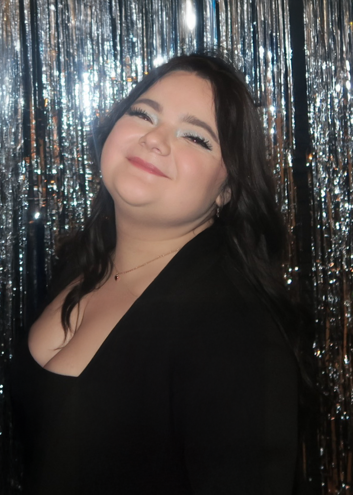 A woman with dark hair and makeup smiling in front of a shiny, metallic fringe backdrop.