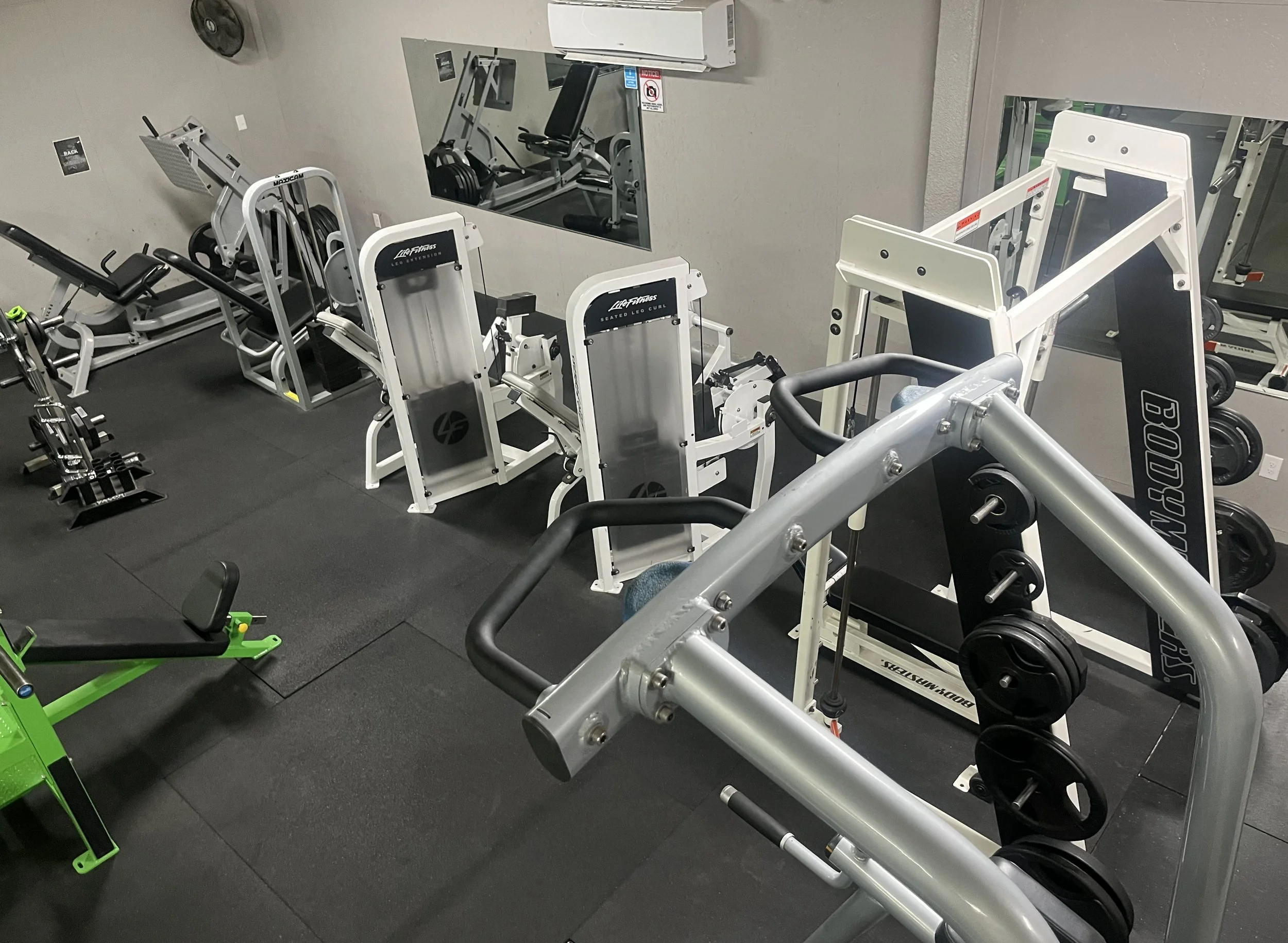  gym with various workout equipment including weight machines, a bench, and dumbbells, with mirrors on the wall. 