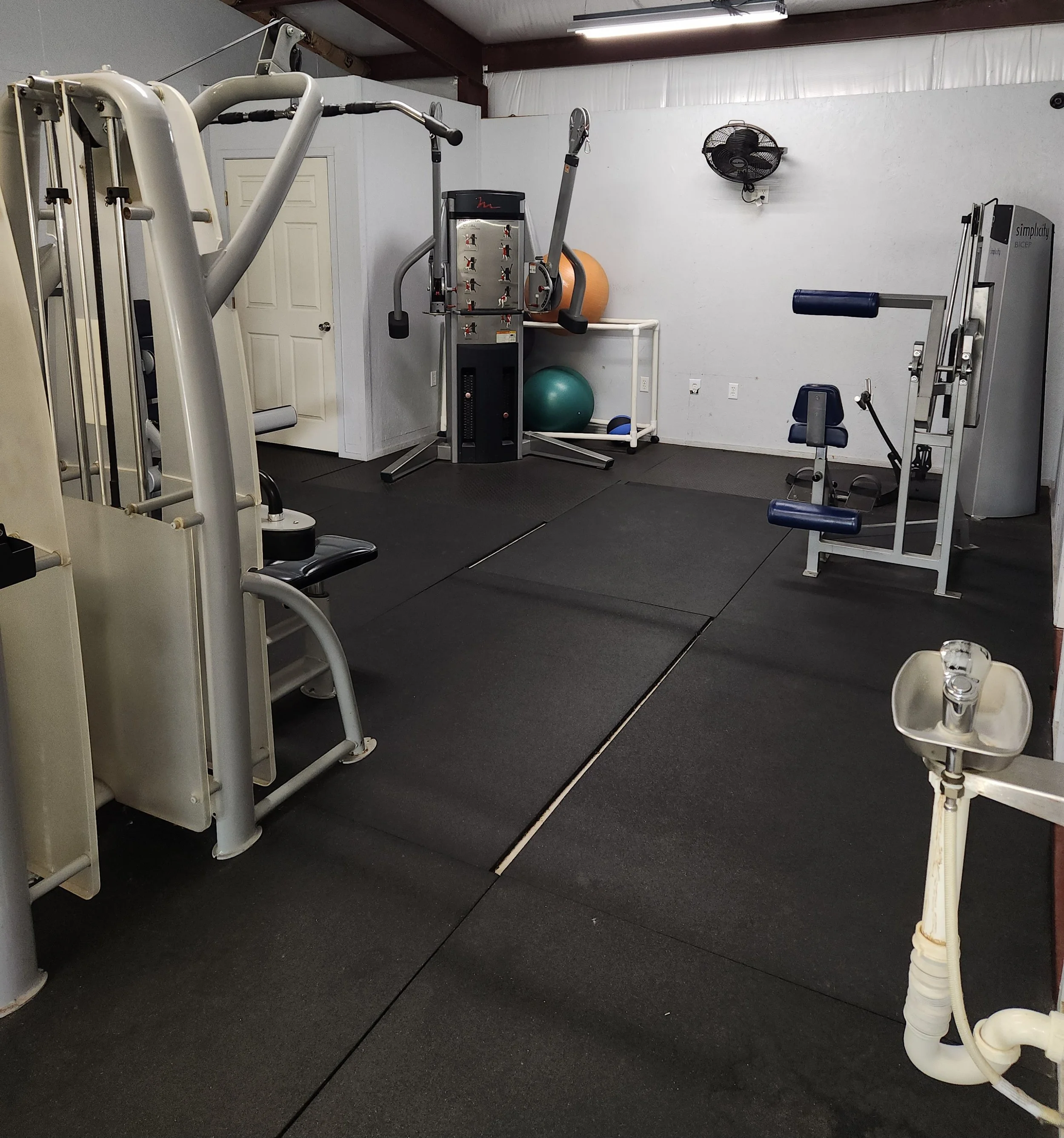 A small gym with various exercise equipment, including weight machines, stability balls, and a water fountain.