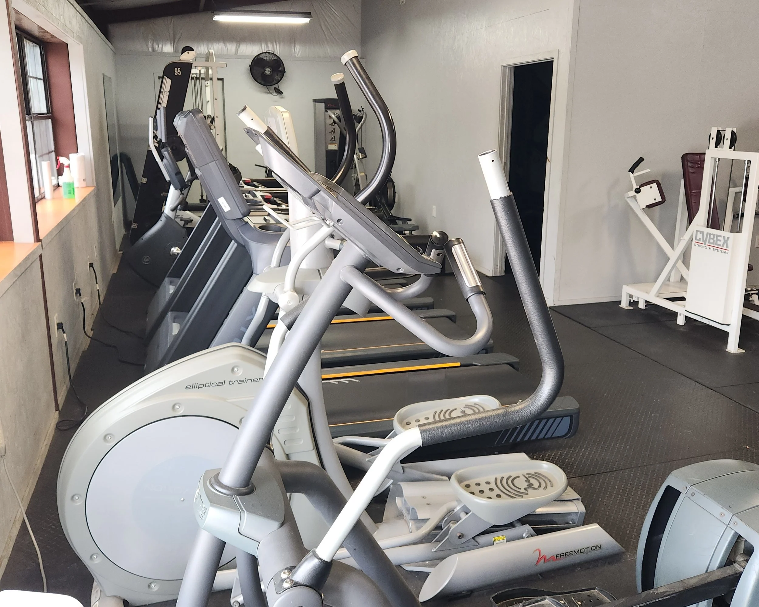 Row of exercise equipment including treadmills, elliptical machines, and a leg press machine in a gym.