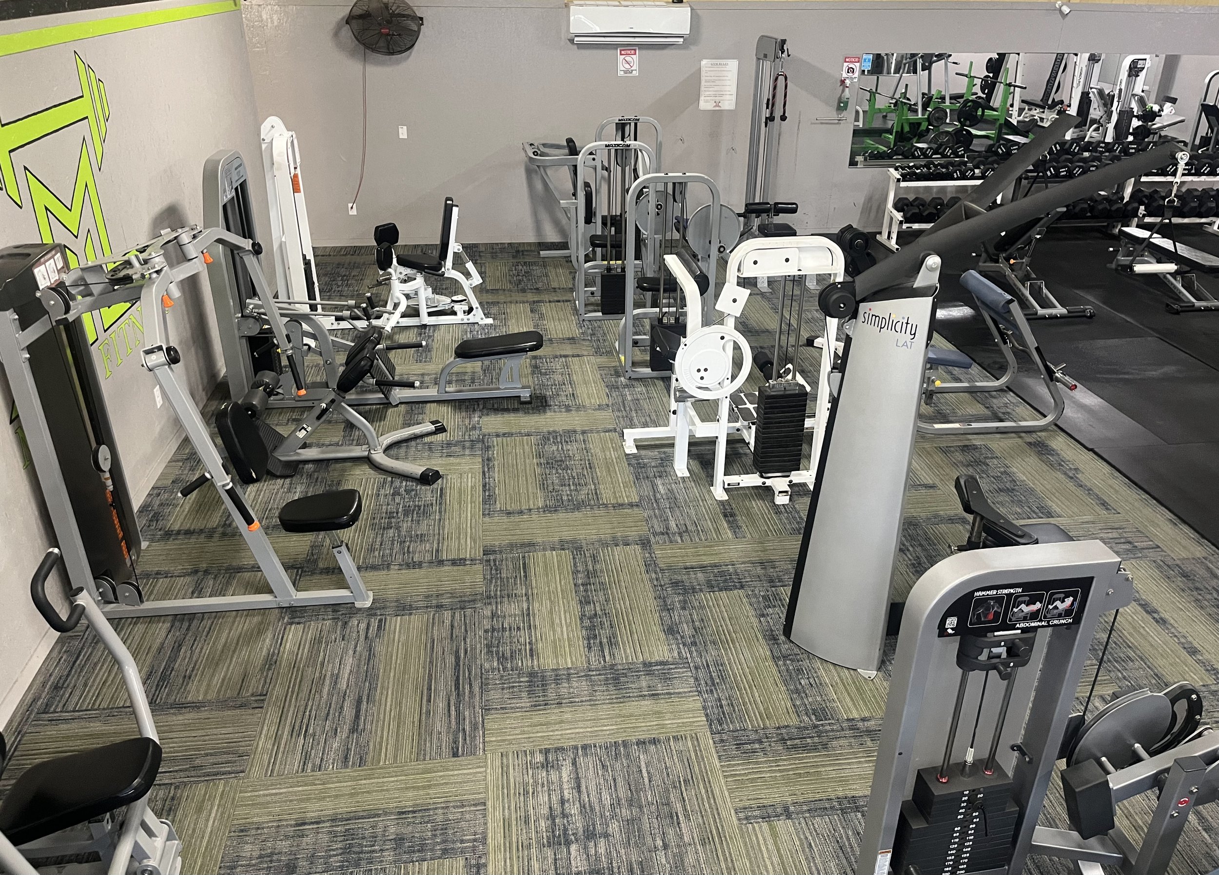 Empty gym with various fitness equipment including weight machines, free weights, and exercise mats.