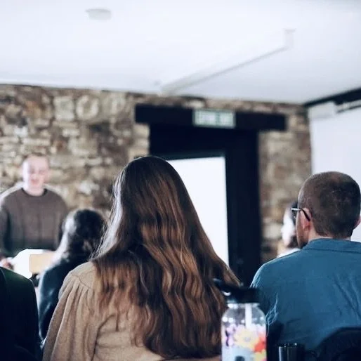 People attending a presentation or lecture in a room with exposed brick walls and a large screen.