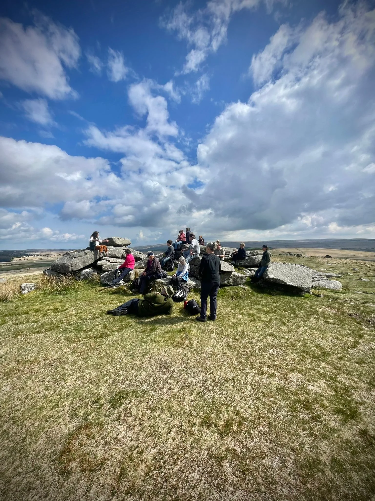 Group of people sitting on a Dartmoor tor under a partly cloudy sky.
