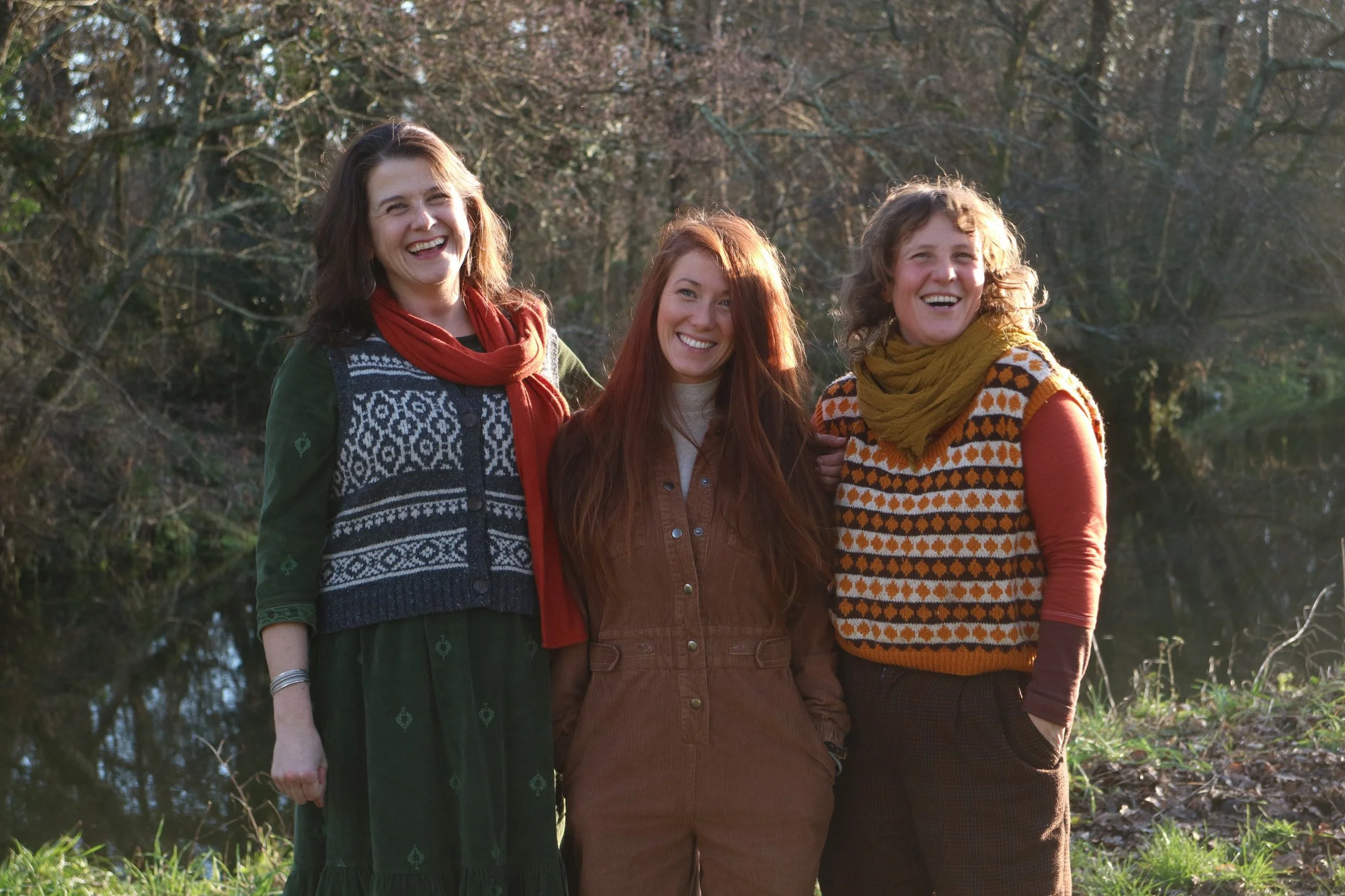 Three women, including Lisa Schneidau on the left, smiling outdoors near a body of water with trees in the background