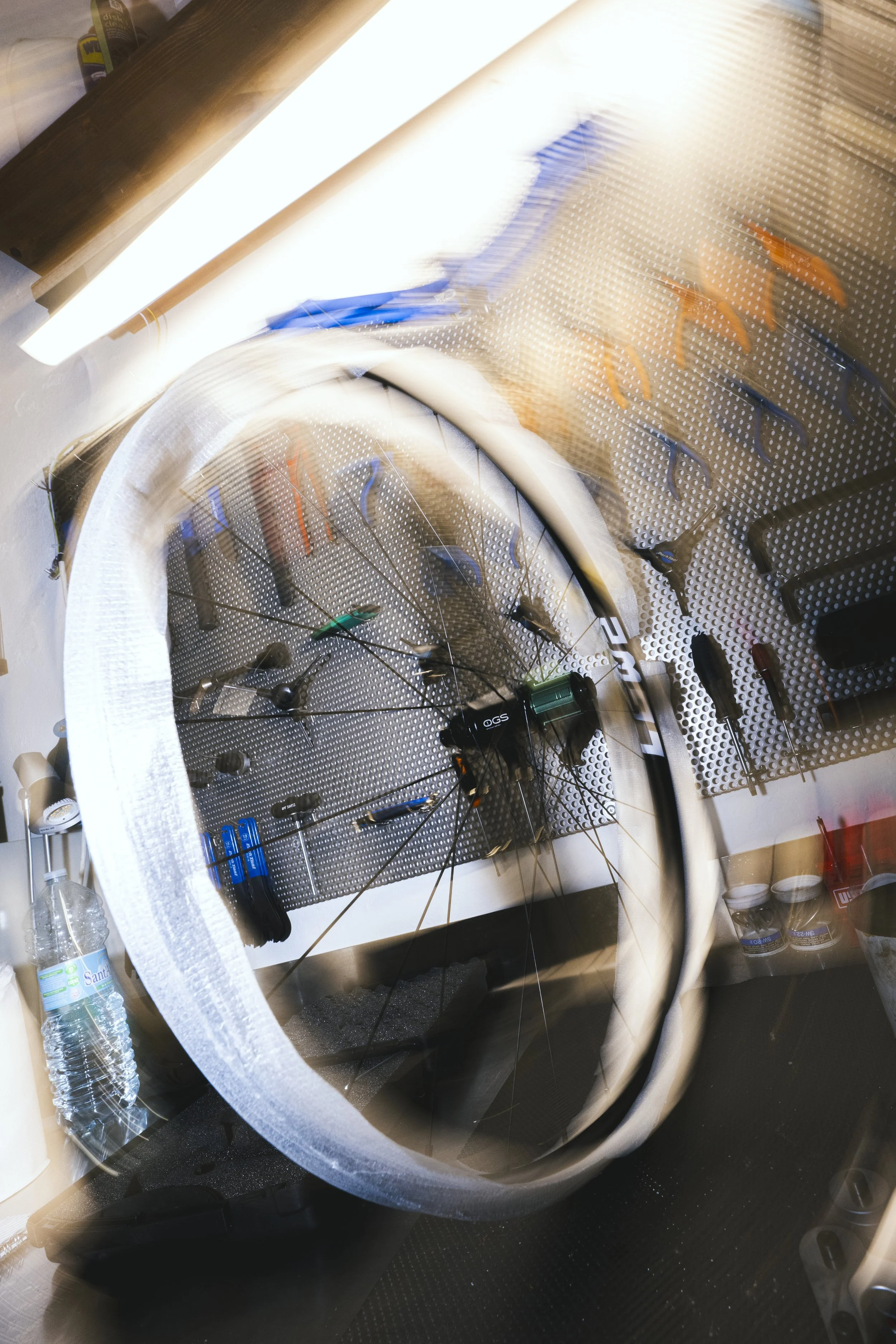 Bici da corsa con ruota anteriore rimossa appoggiata in un garage o officina, con attrezzi da riparazione appesi alla parete.