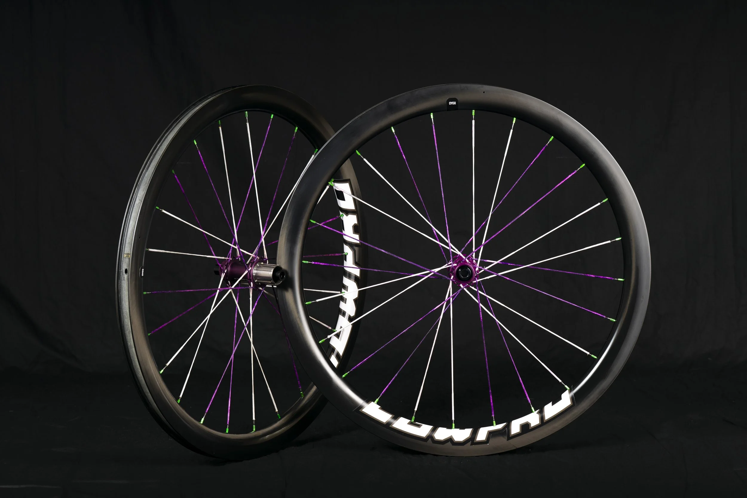 Due ruote di bicicletta con raggi colorati, una con pneumatico e l'altra senza, in posa su sfondo nero.