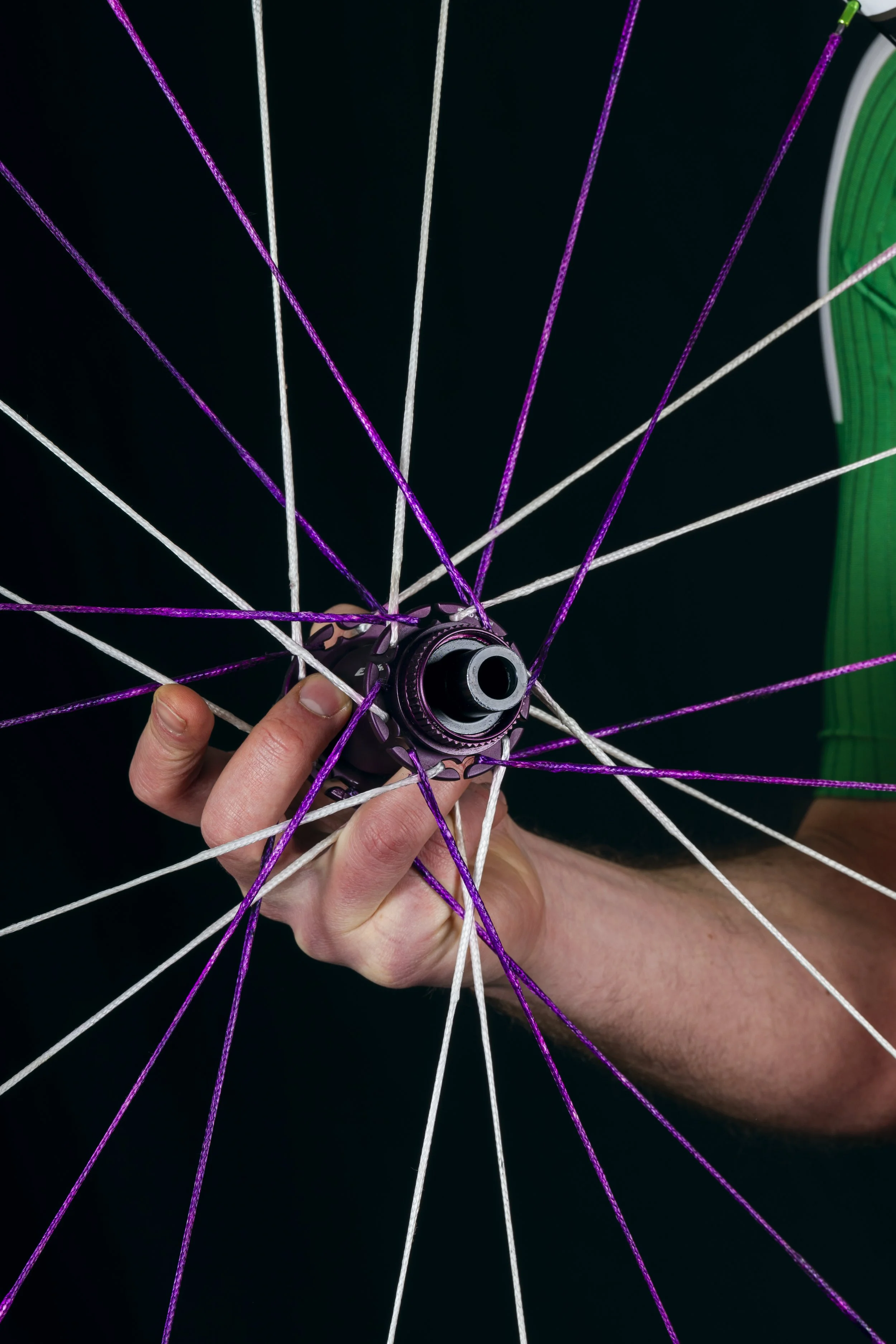 Zoom su una mano che tiene un mozzo di bicicletta con raggi di colore viola e bianco attaccati ai fori, con uno sfondo nero