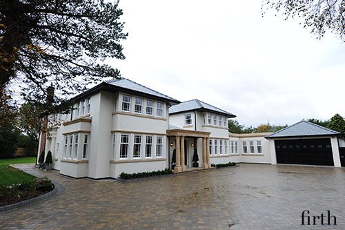 Large white two-story house with black roof and attached garage, surrounded by trees and a paved driveway.