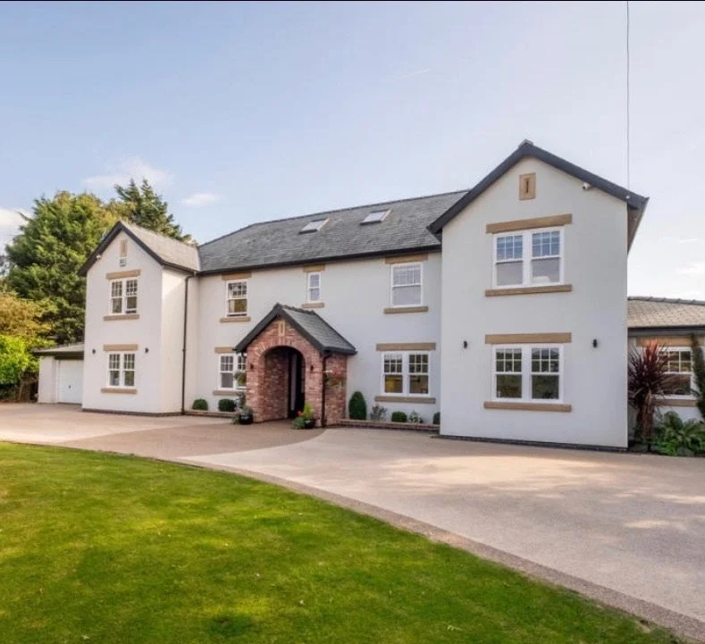 Large white house with grey roof and brick archway entrance, surrounded by a driveway and lawn.