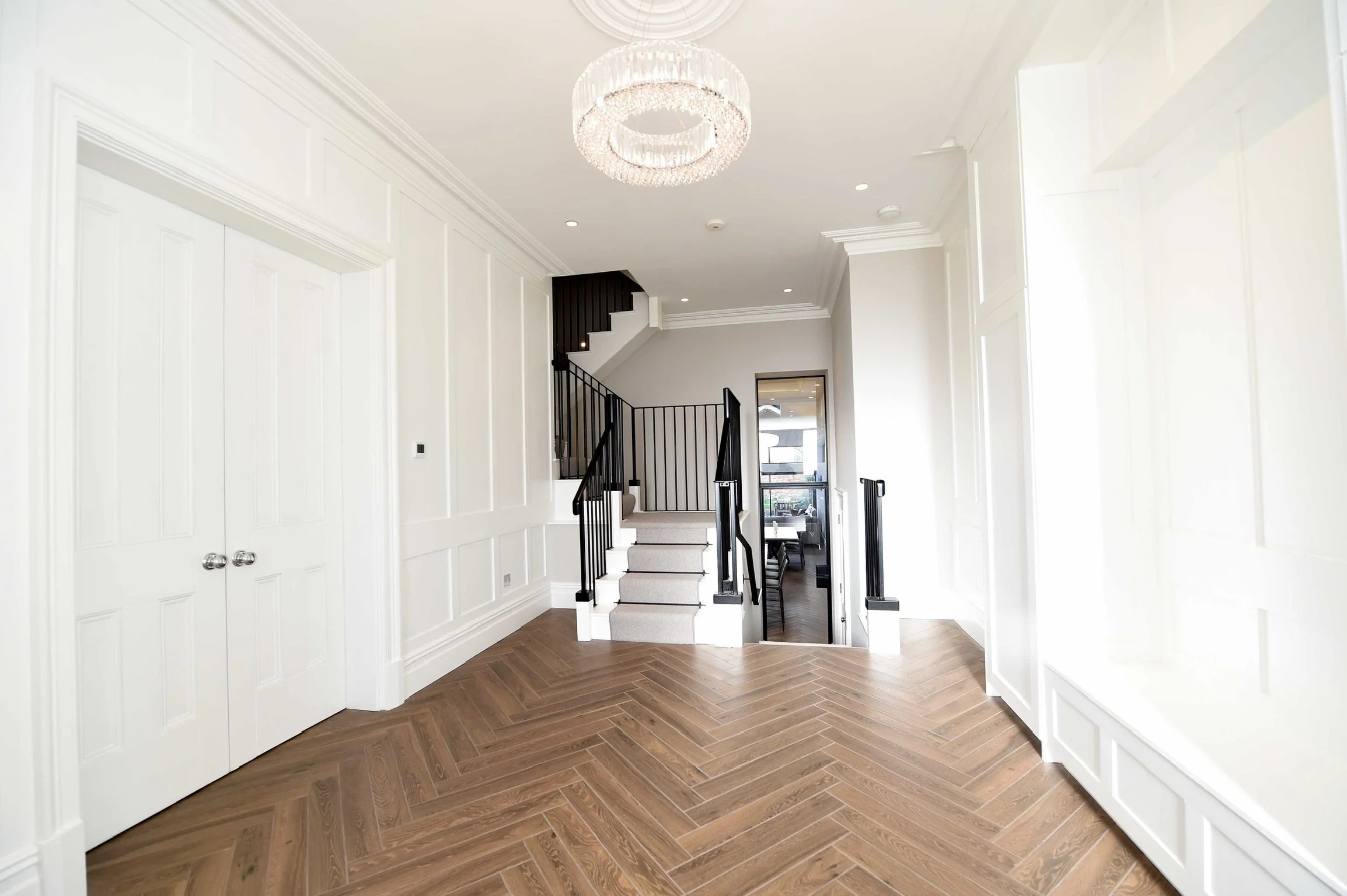 Bright foyer with white walls, a modern chandelier, a staircase with black railings, and a glass door leading to a dining area.