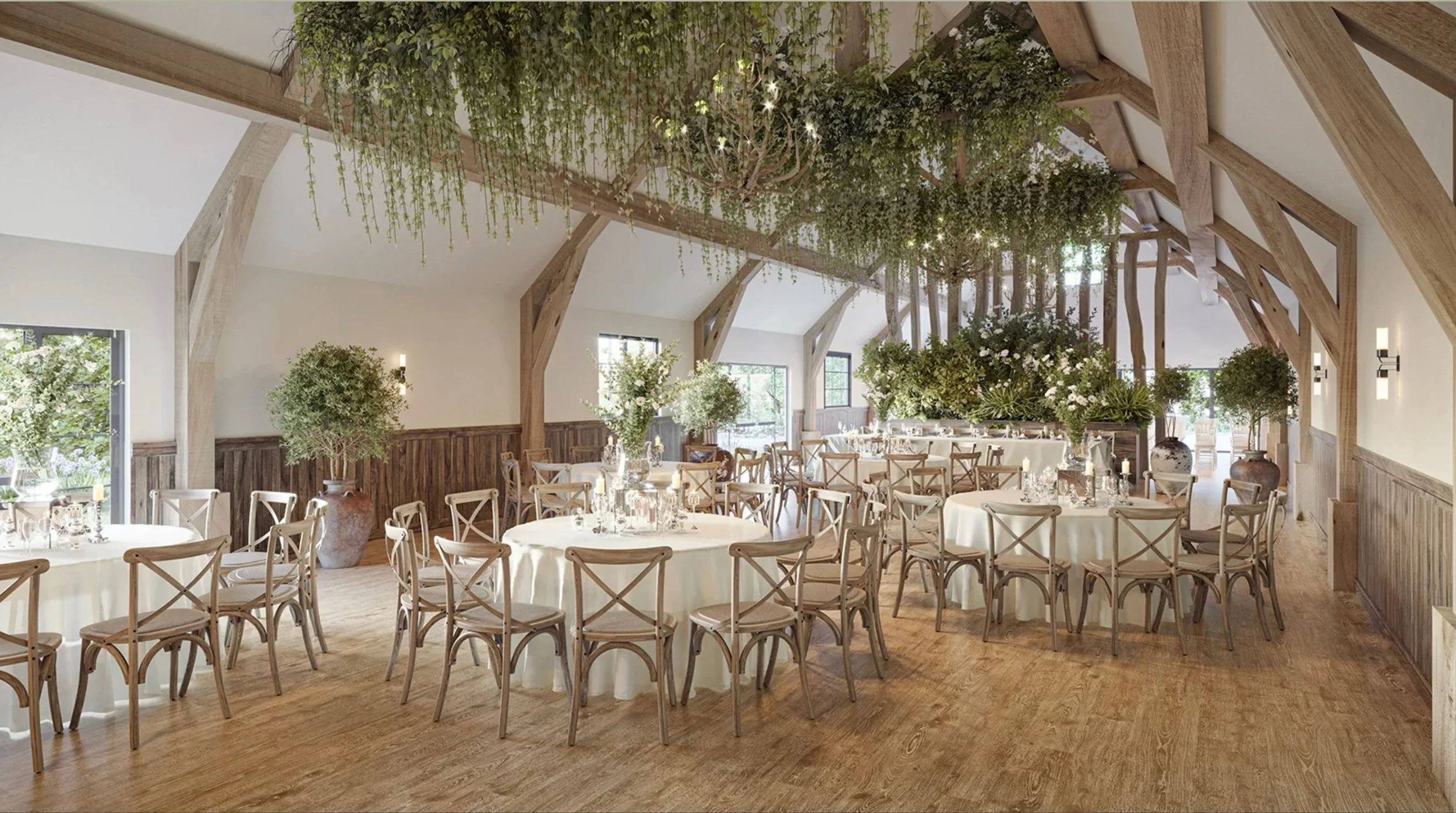 Elegant event venue with round tables covered in white tablecloths, set with glassware and floral centerpieces, surrounded by beige chairs with cross-back designs, decorated with large potted plants and greenery, under a vaulted ceiling with exposed 