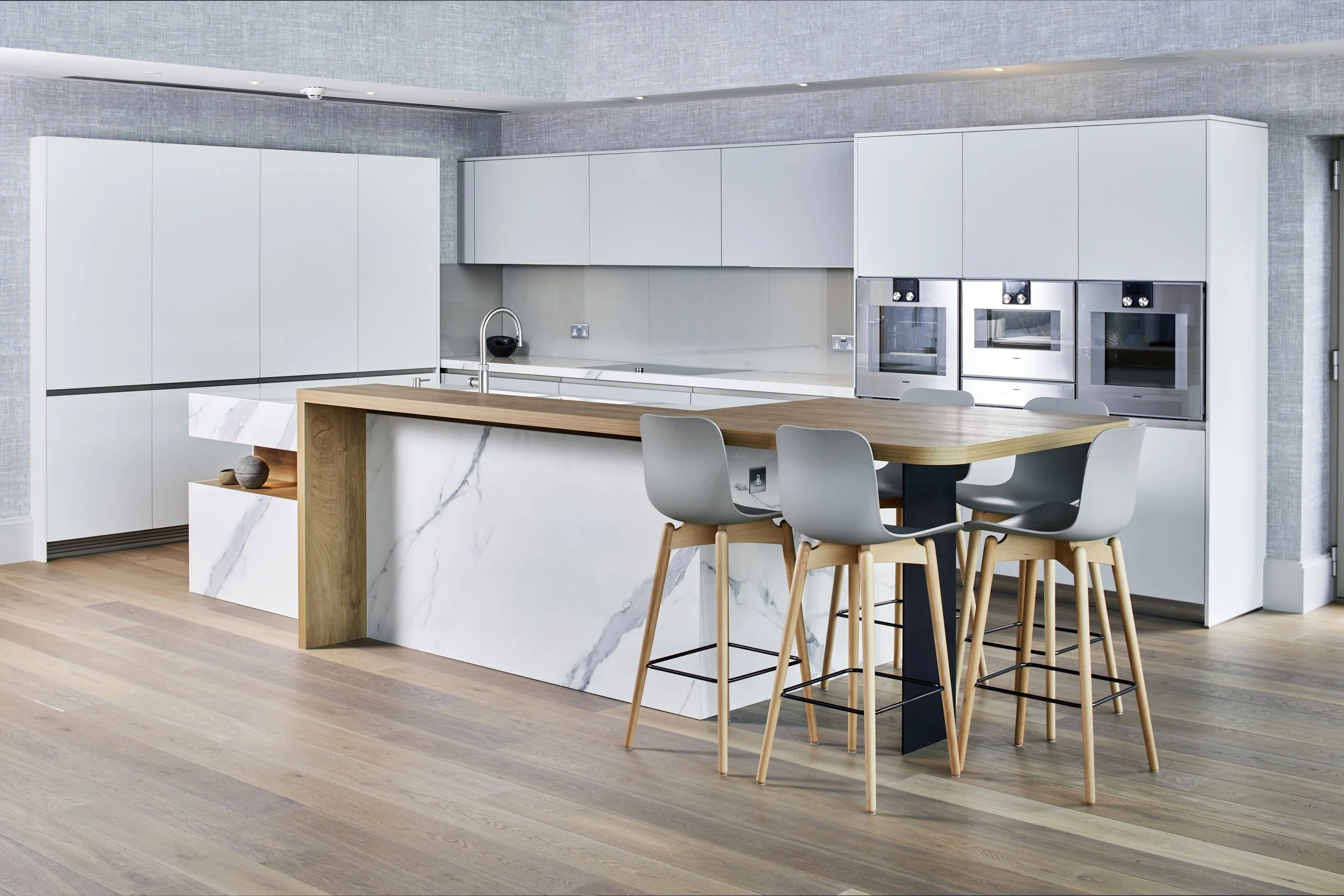 Modern kitchen with white cabinets, a marble island, and a wooden dining table with four gray chairs.