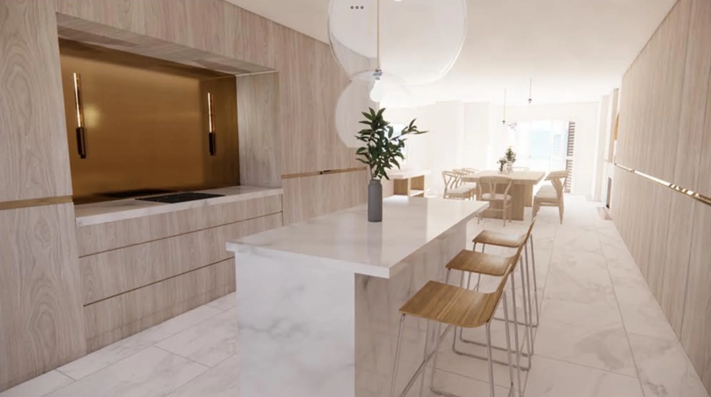 A modern kitchen and dining area with light wood cabinetry, a white marble island, three wooden bar stools, a round dining table with chairs, and a vases with green leaves, all illuminated by ample natural light.