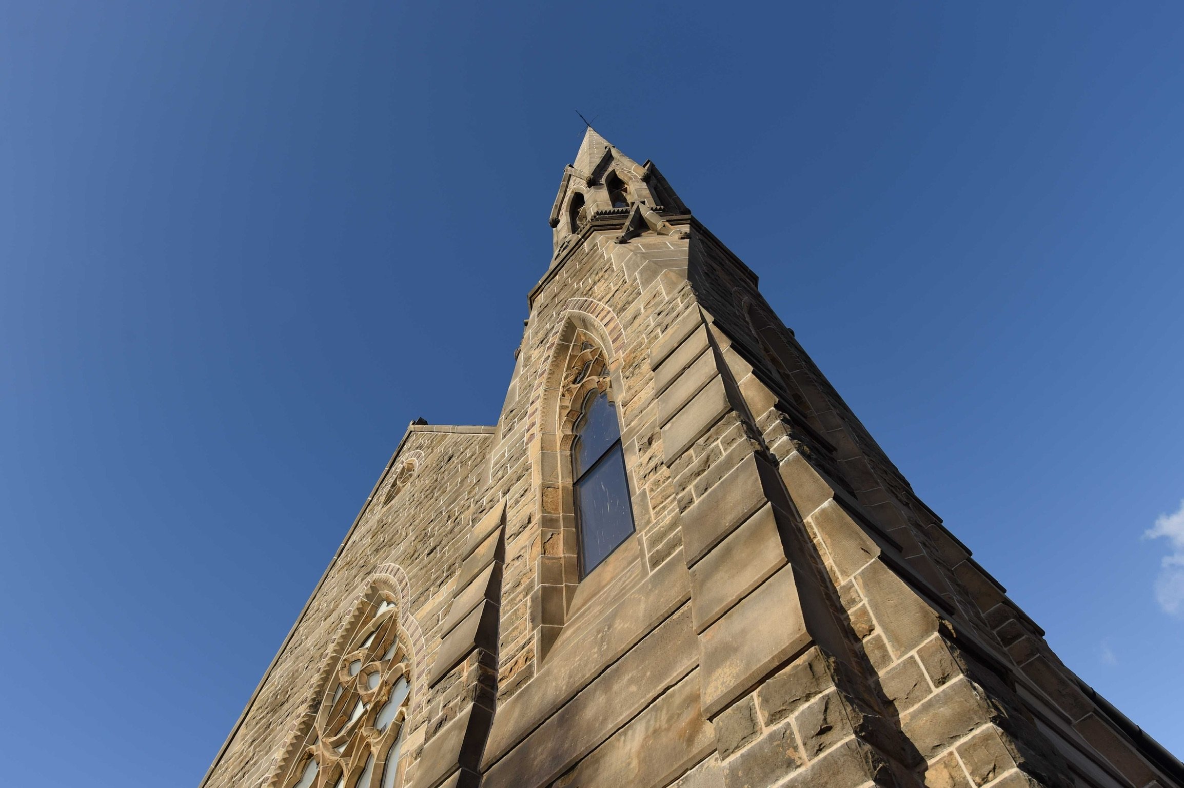Low-angle view of a tall stone church steeple against a clear blue sky.